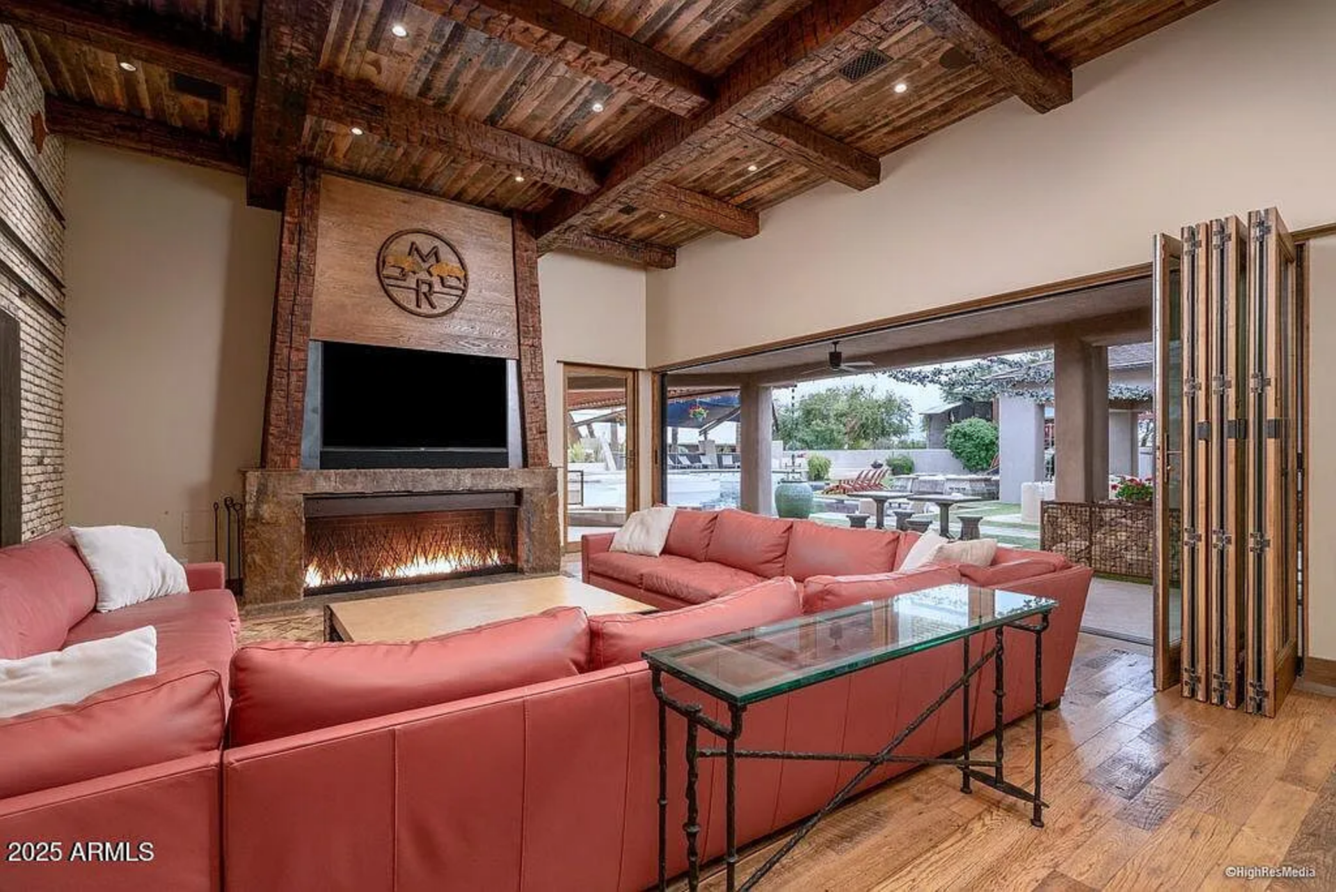 The seating arrangement faces a tall fireplace wrapped in stone and dark metal, topped with a mounted television and a custom emblem that adds a personal touch to the space.