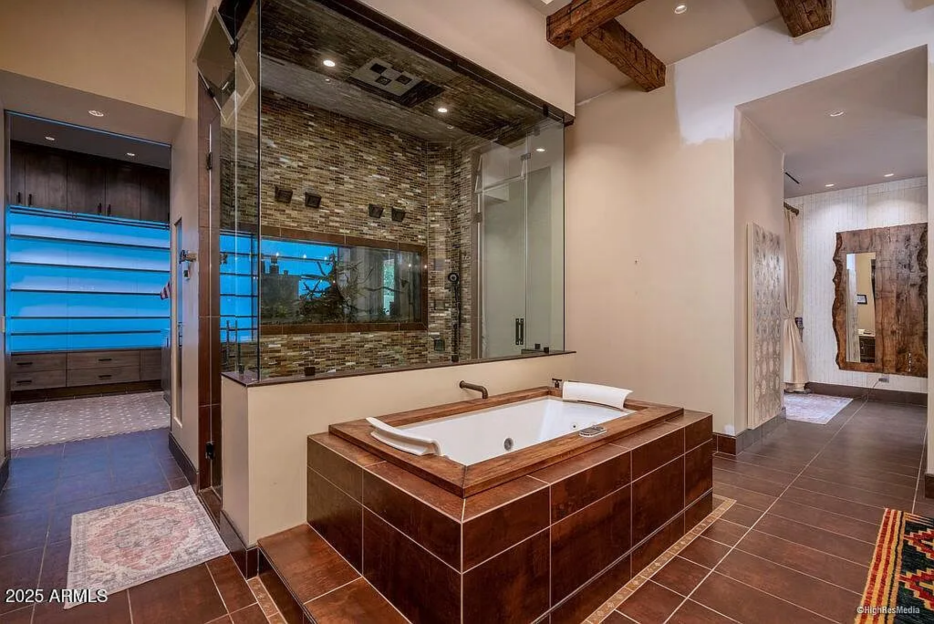 At the center of the room, a deep soaking tub is framed in wood and tile, positioned beside a glass-enclosed shower wrapped in stacked stone.