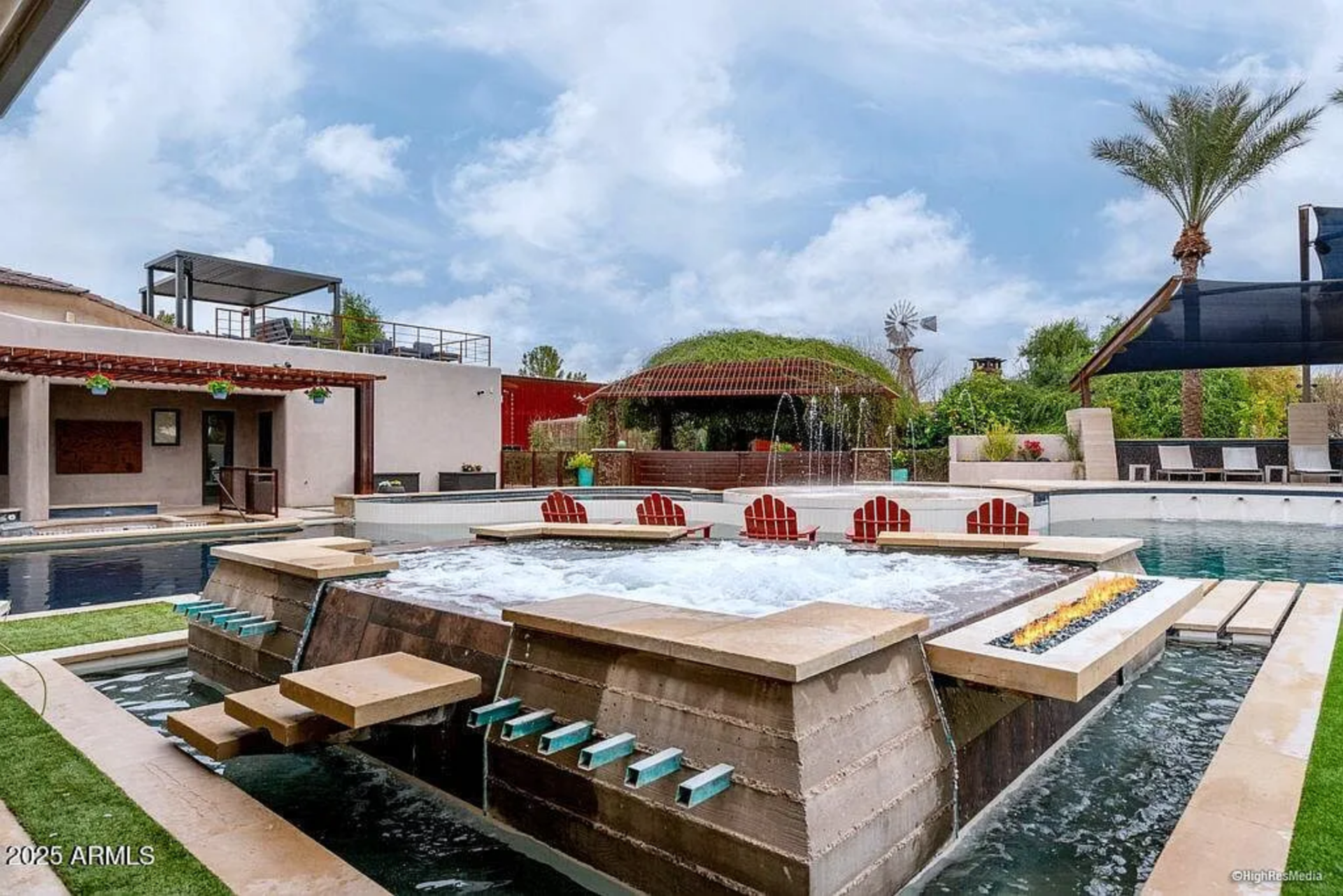 In the center is a raised spa, surrounded by red Adirondack-style chairs set partially in the water for a true resort-style soaking experience as water features spill over the edges.