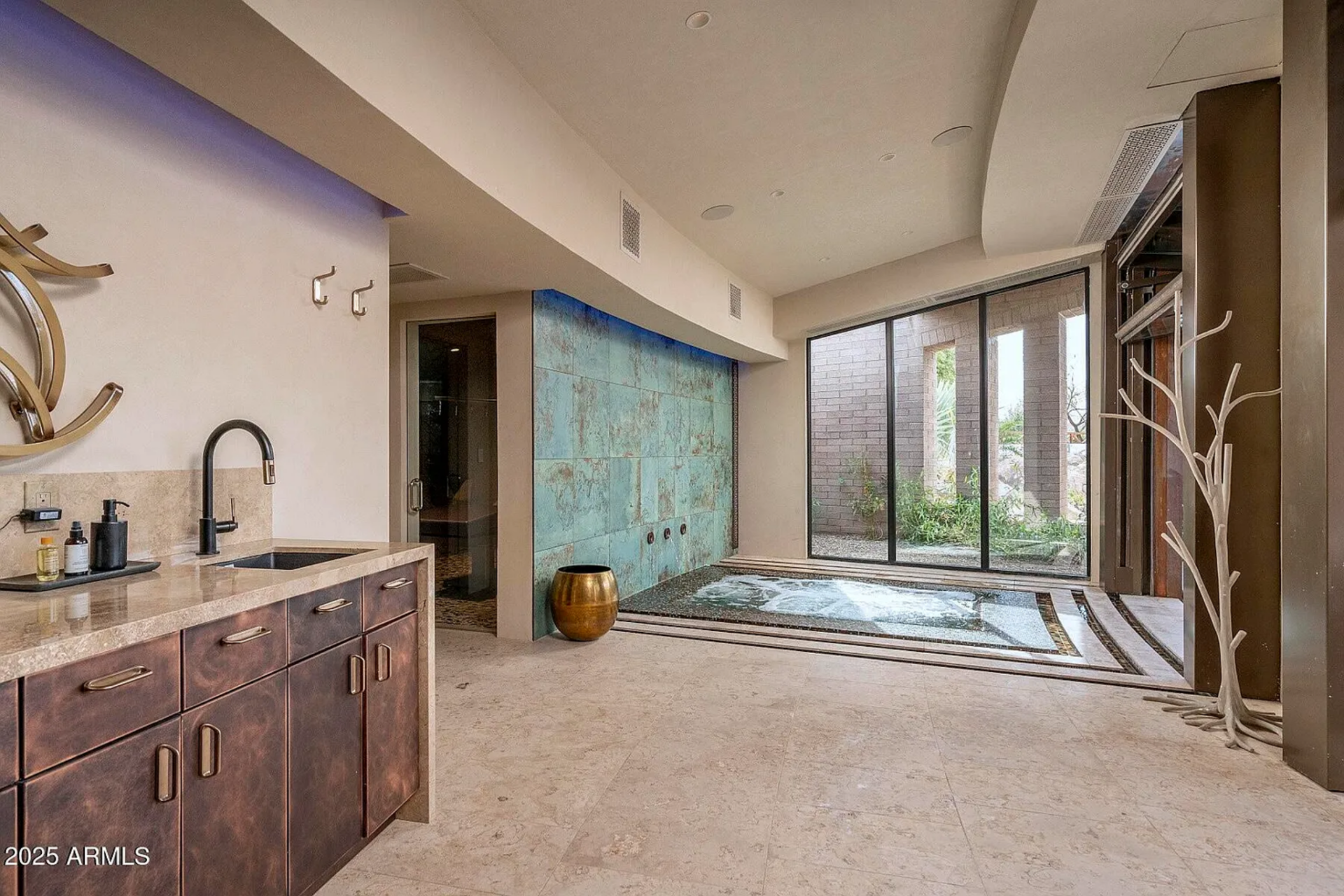 The spa’s in-ground hot tub is built into a peaceful indoor setting, surrounded by stone and glass, with a full wall water feature that adds movement and sound.