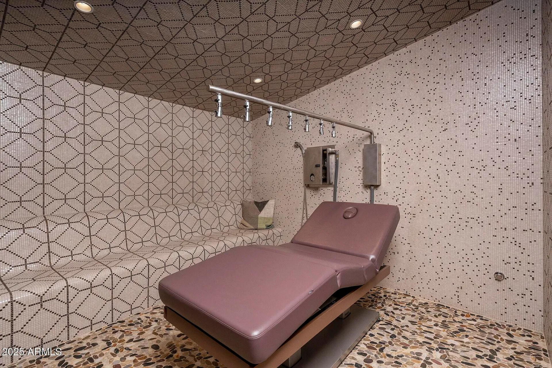 The steam room is fully wrapped in geometric mosaic tile, with built-in bench seating and multiple overhead steam outlets.