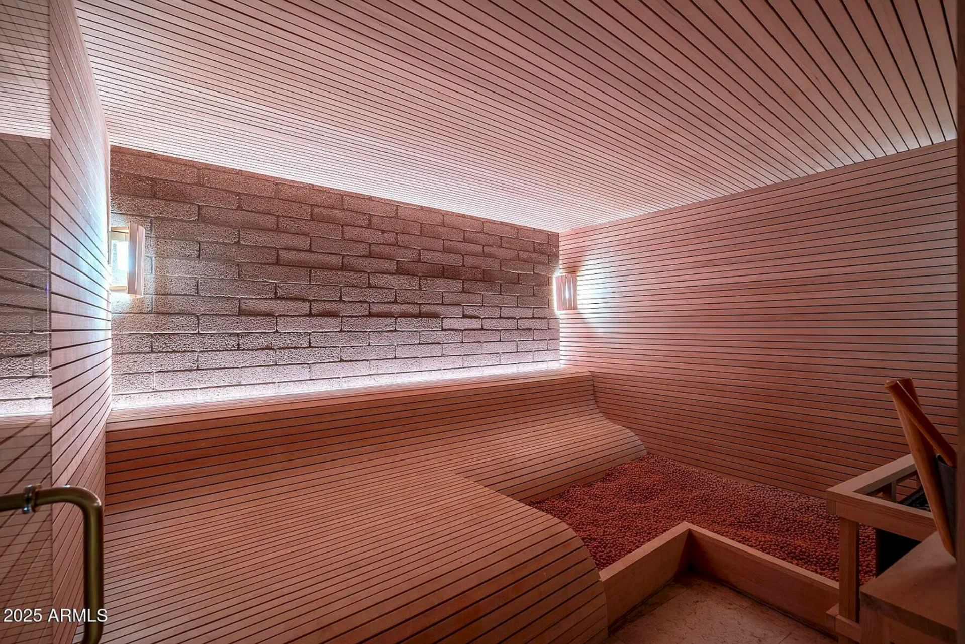 The sauna is lined in horizontal wood slats with tiered bench seating and soft backlighting along the brick accent wall.