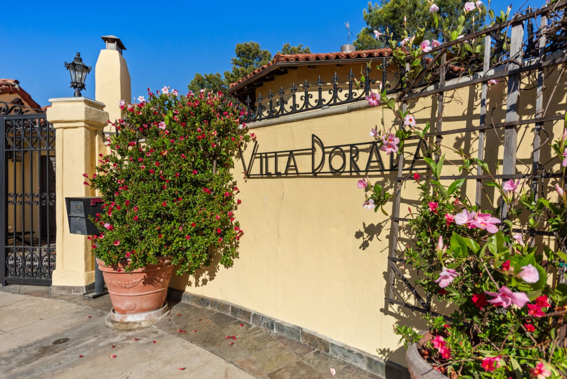Villa Dorada remains a preserved example of Spanish Revival architecture, its butter-yellow stucco walls, red clay tile roof, and wrought-iron detailing still sharply defined against the blue sky.