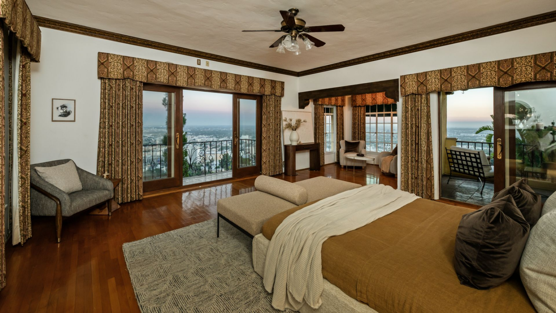 Across two walls, French doors open directly to two different balconies, extending the suite outward, while an indoor sitting area is positioned between them, creating a layered layout.