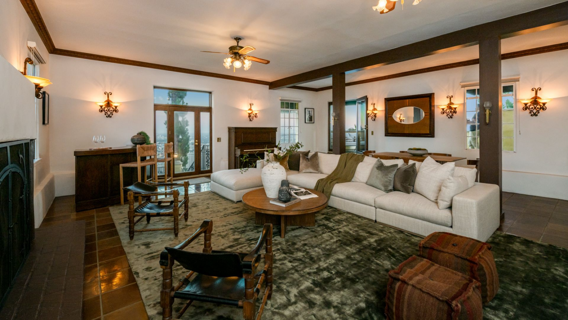 At the center of the room, a large sectional and a round wood coffee table define the main seating area, positioned to face both the fireplace and the exterior doors.