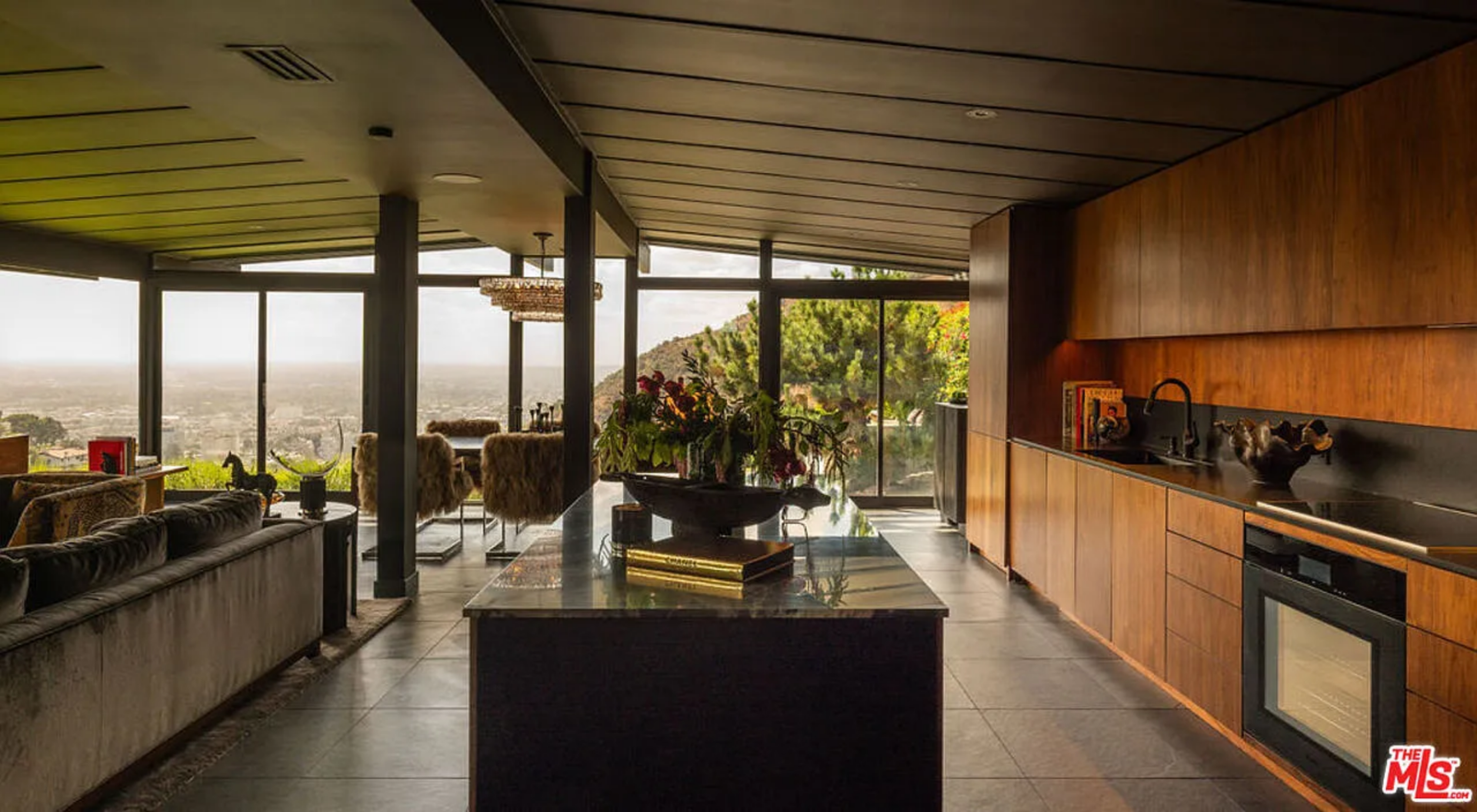 From the island, the space opens directly to the glass walls, allowing the cooking area to share the same hillside backdrop as the living room.