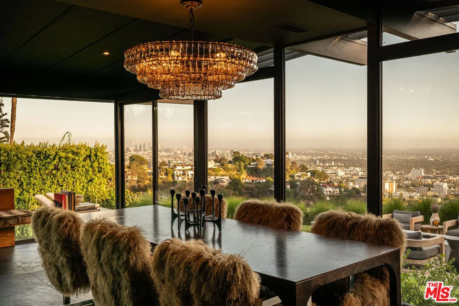 Within the space, a long rectangular table is centered beneath a tiered chandelier, and is surrounded by dining chairs wrapped in textured upholstery.