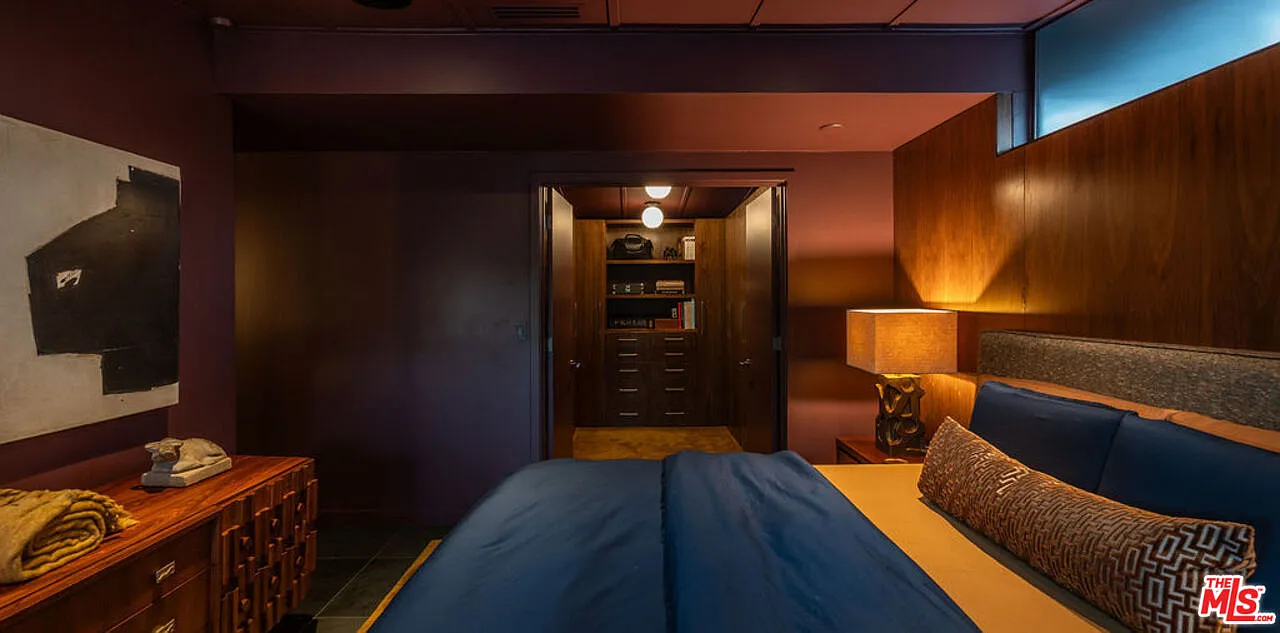 A wide opening leads from the sleeping area into a walk-in closet with built-in cabinetry and shelving that matches the dark palette of the bedroom.
