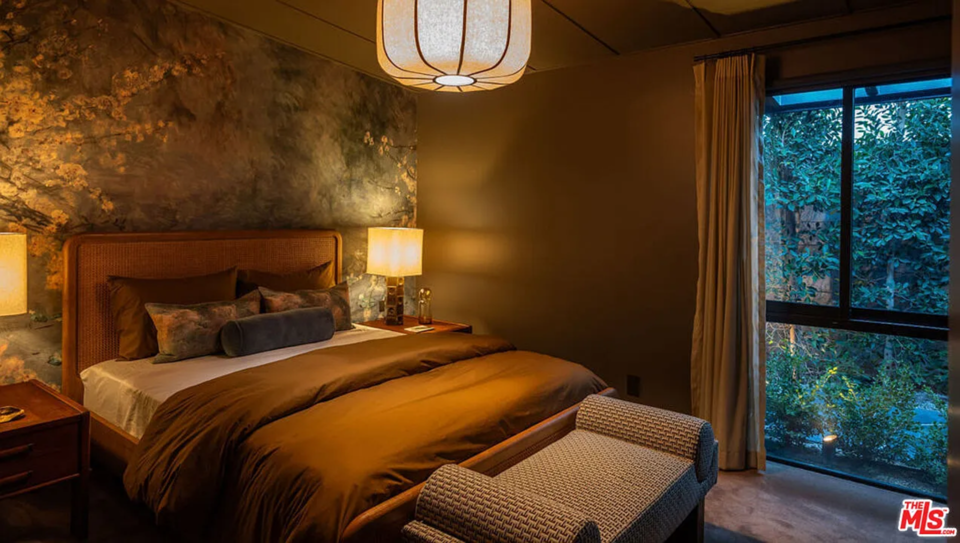 Set against a large-scale mural behind the bed, this room centers on a woven cane headboard framed by matching wood nightstands.