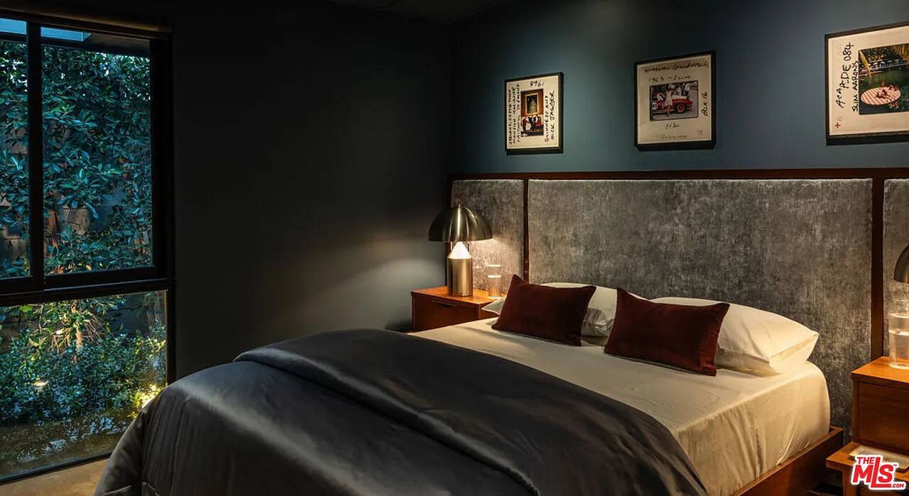 Wrapped in deep blue walls, this bedroom features a paneled, upholstered headboard that stretches horizontally across the wall.