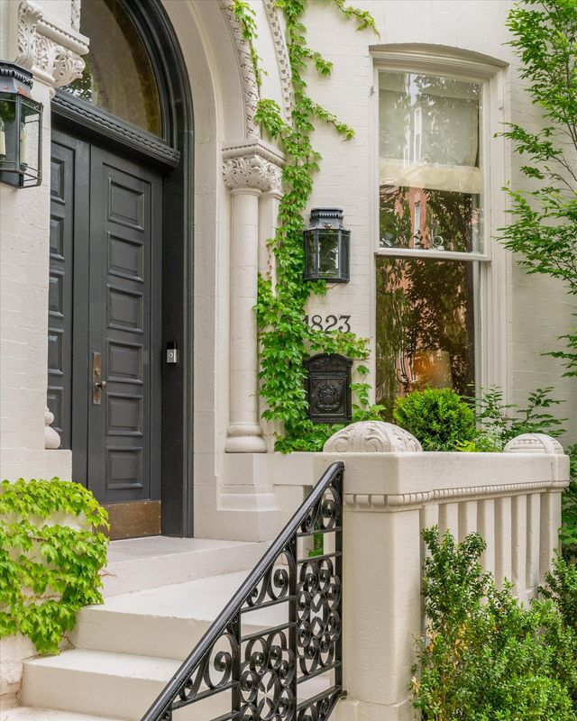 The entrance to Chris Hughes’ historic Washington, D.C. mansion has ivy climbing the light brick exterior, framing an arched black door with carved stone detailing and traditional lantern sconces.