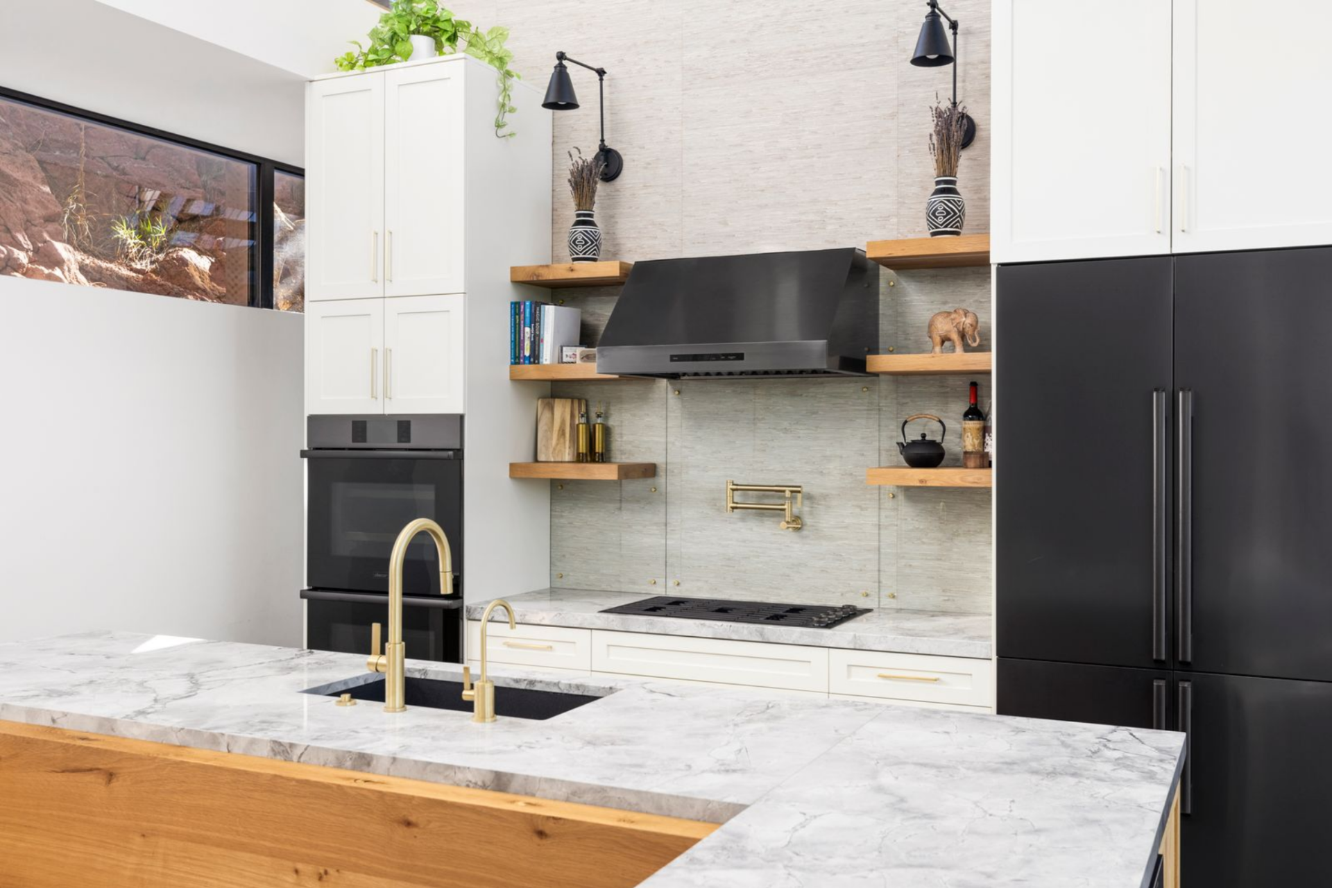 A sculptural stone backsplash rises behind the range, framed by floating wood shelves that soften the clean lines while adding warmth and display space. 