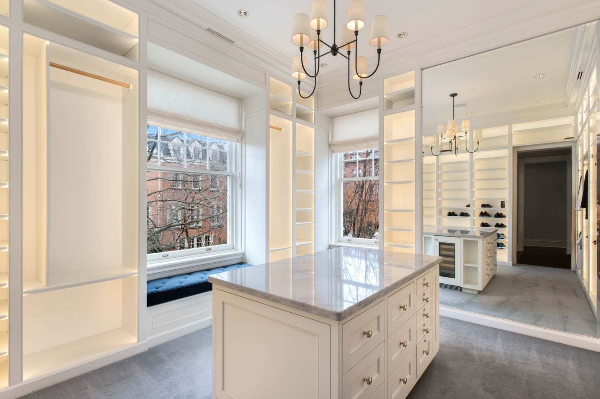Floor-to-ceiling cabinetry, illuminated shelving, integrated drawers, and a central island define the layout, while a mirrored wall lets you check your outfit.