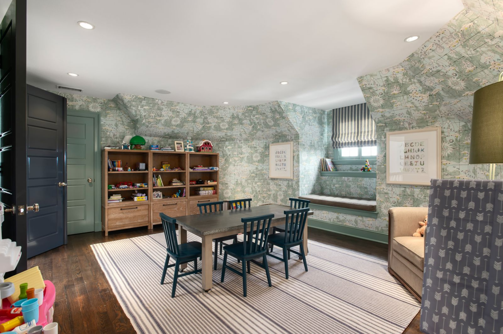 Along one wall, open wood shelving keeps books and toys visible and accessible, while a reading chair and floor lamp establish a quieter corner opposite the play area.