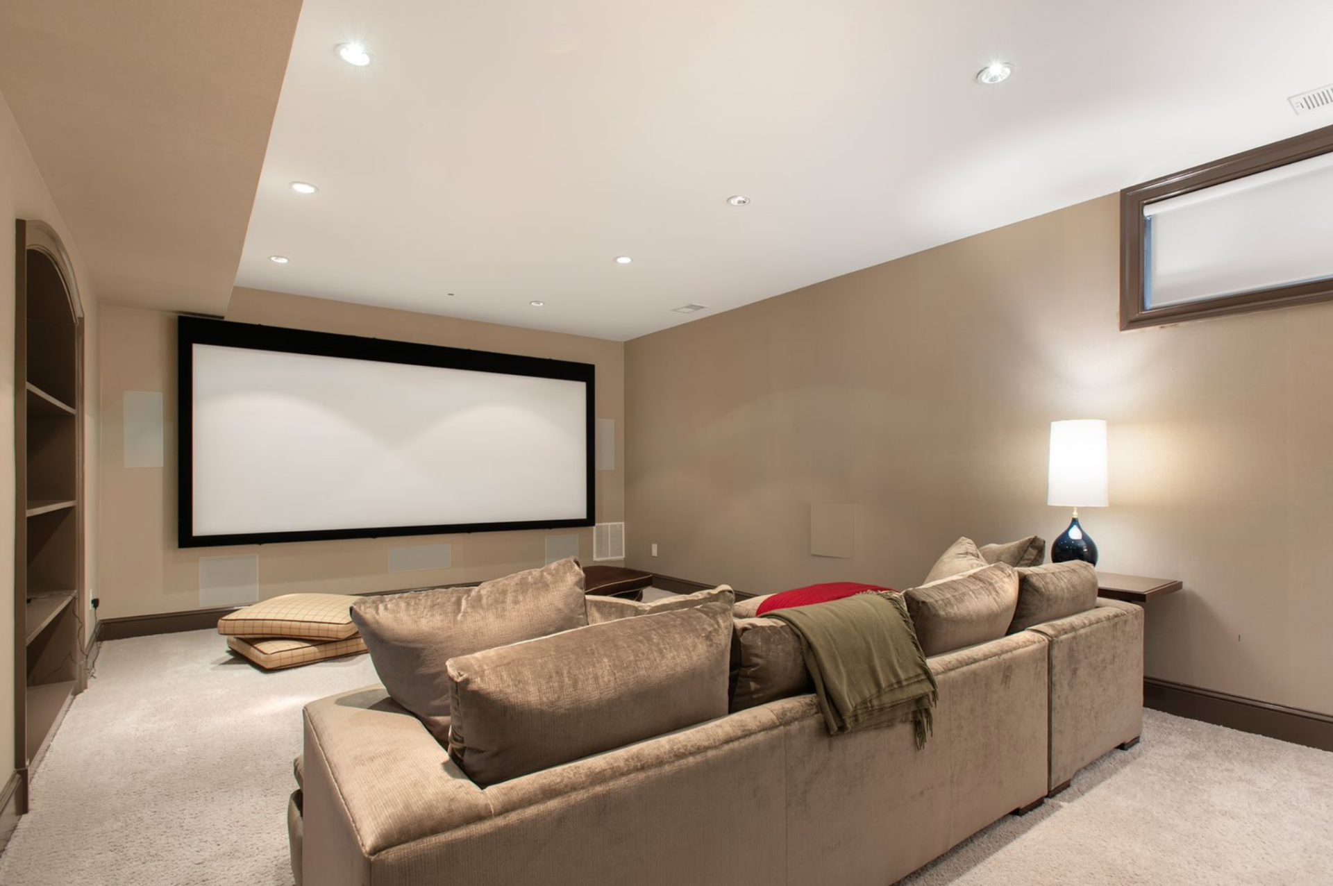 Featuring a wall-mounted projection screen framed in black, the media room is arranged with a deep sectional positioned directly opposite the screen. 