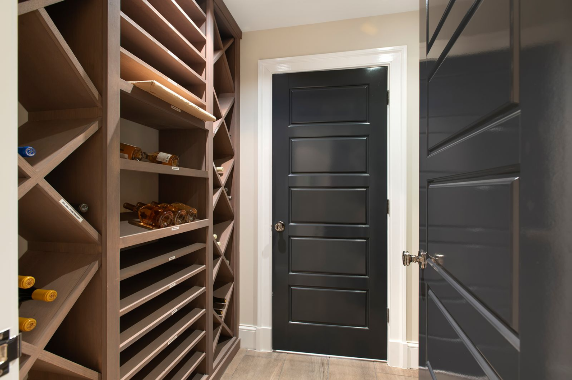 The wine cellar is enclosed with custom wood racking that climbs from floor to ceiling, and individual slots labeled for organization, offering both horizontal shelving and diamond-style bottle storage.