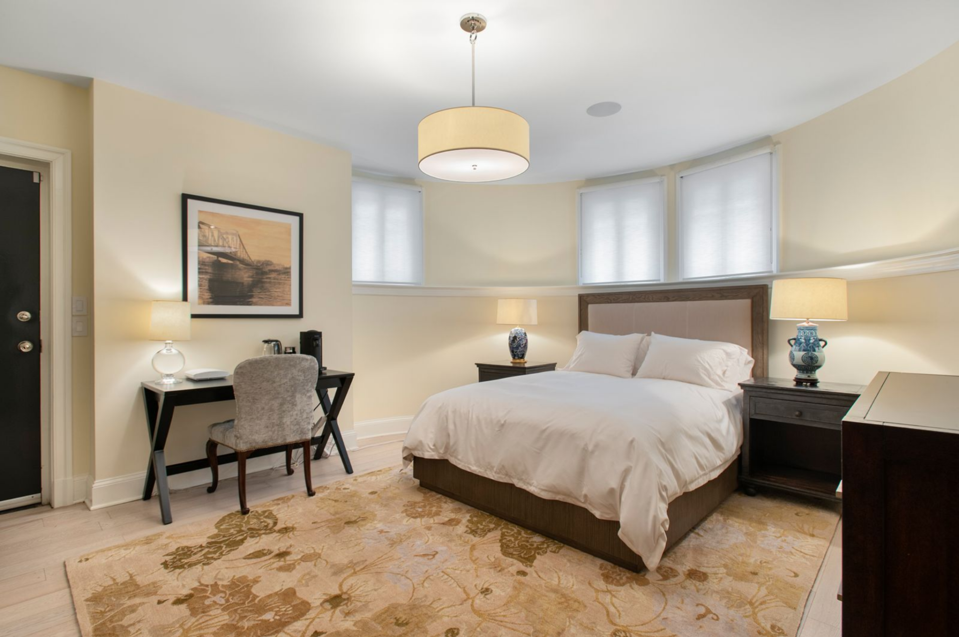 A bed is centered between matching nightstands, while a compact writing desk and beverage station sit along one wall.