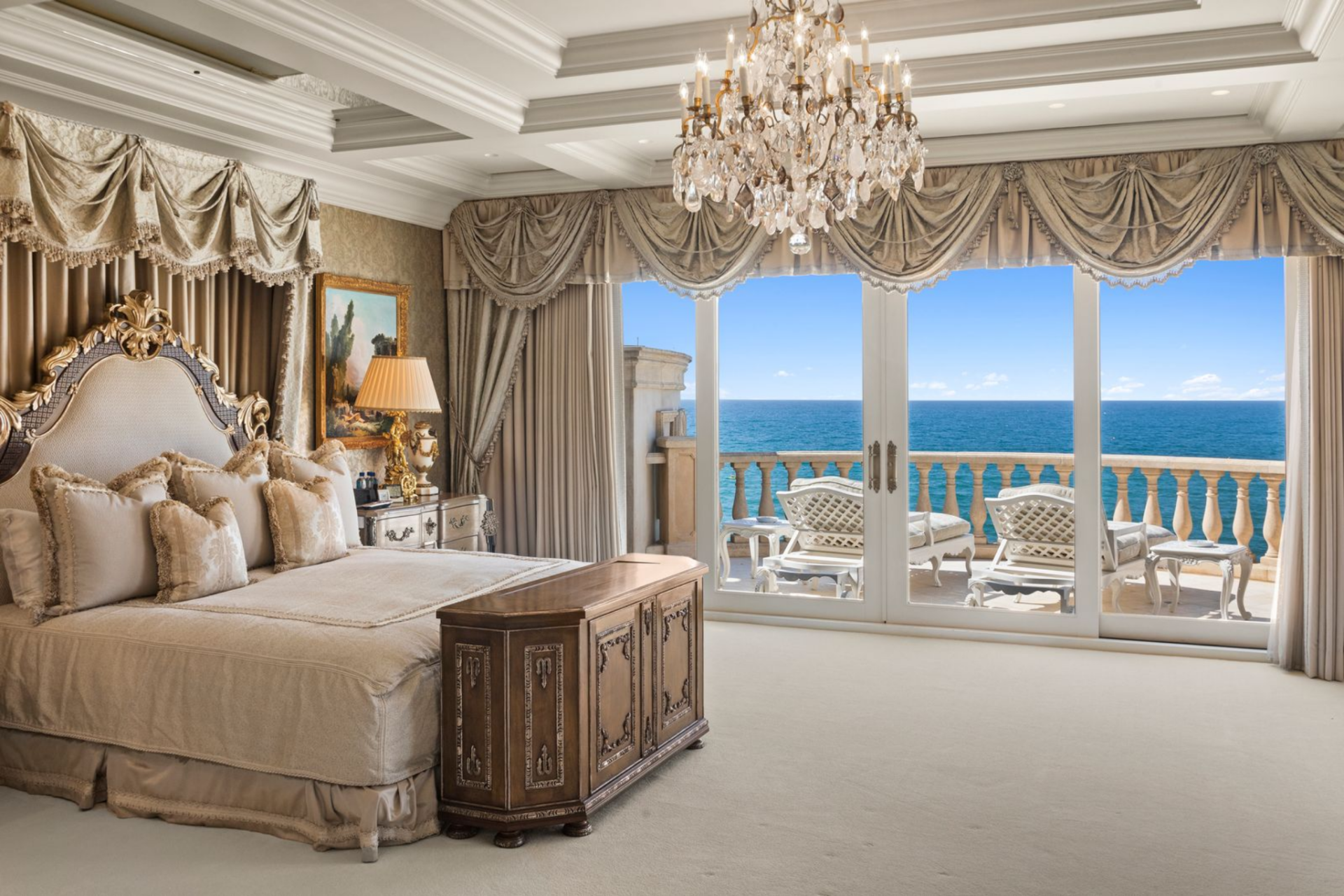 The primary suite in the main house uses heavy, swagged drapery to frame a wall of French doors that open to a private terrace overlooking the water.