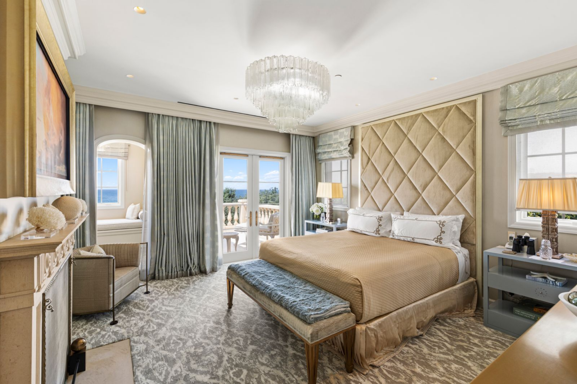 A diamond-tufted upholstered bedframe adds an accent to one wall, and a tiered crystal chandelier introduces a subtle layer of glamour overhead. 
