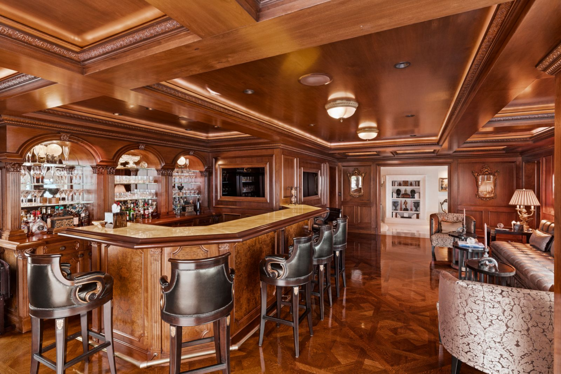 Leather-upholstered bar stools with rolled arms and nailhead trim line the counter, reinforcing the tailored, old-world atmosphere.