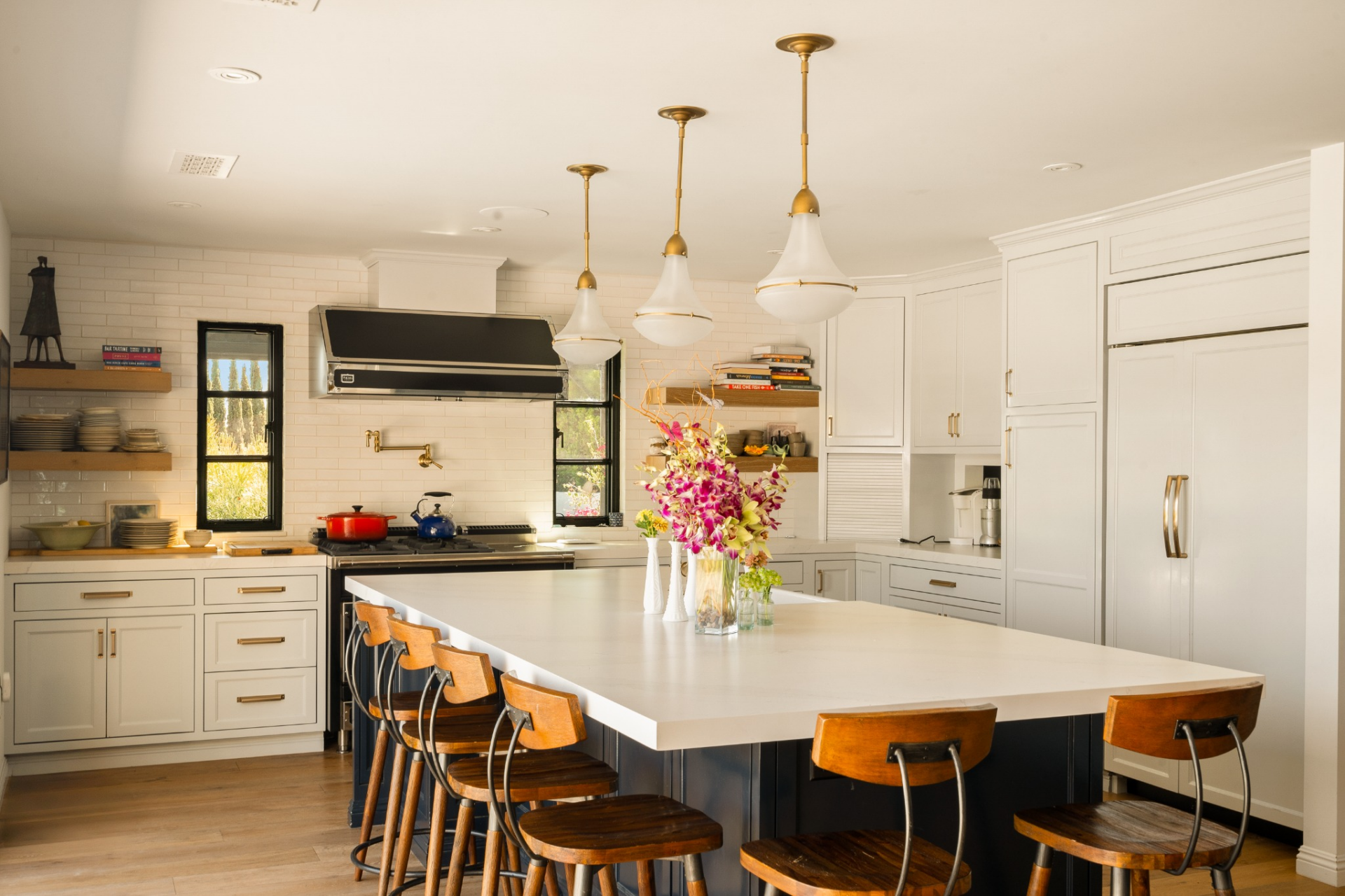 the kitchen opens to a large waterfall island with bar seating, clean white cabinetry with warm wood accents and brass hardware.