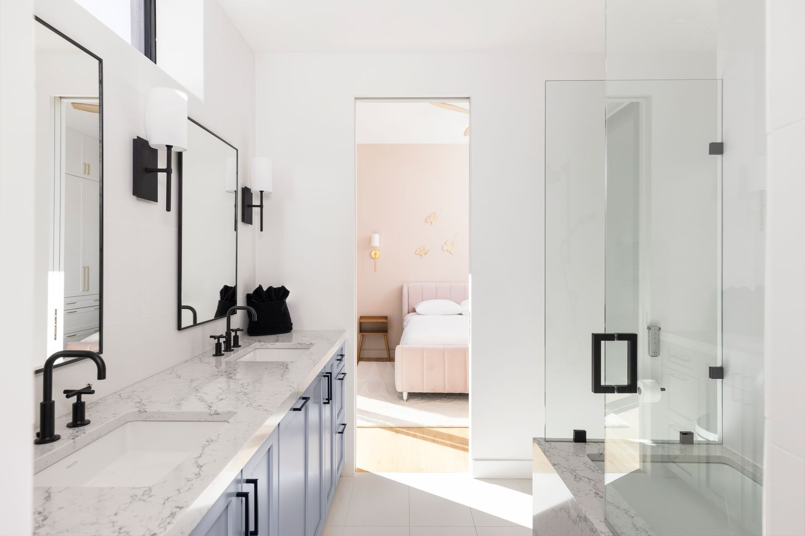 Jack and Jill bathroom with a long double vanity with marble countertops and matte black fixtures across from a glass-enclosed tub.