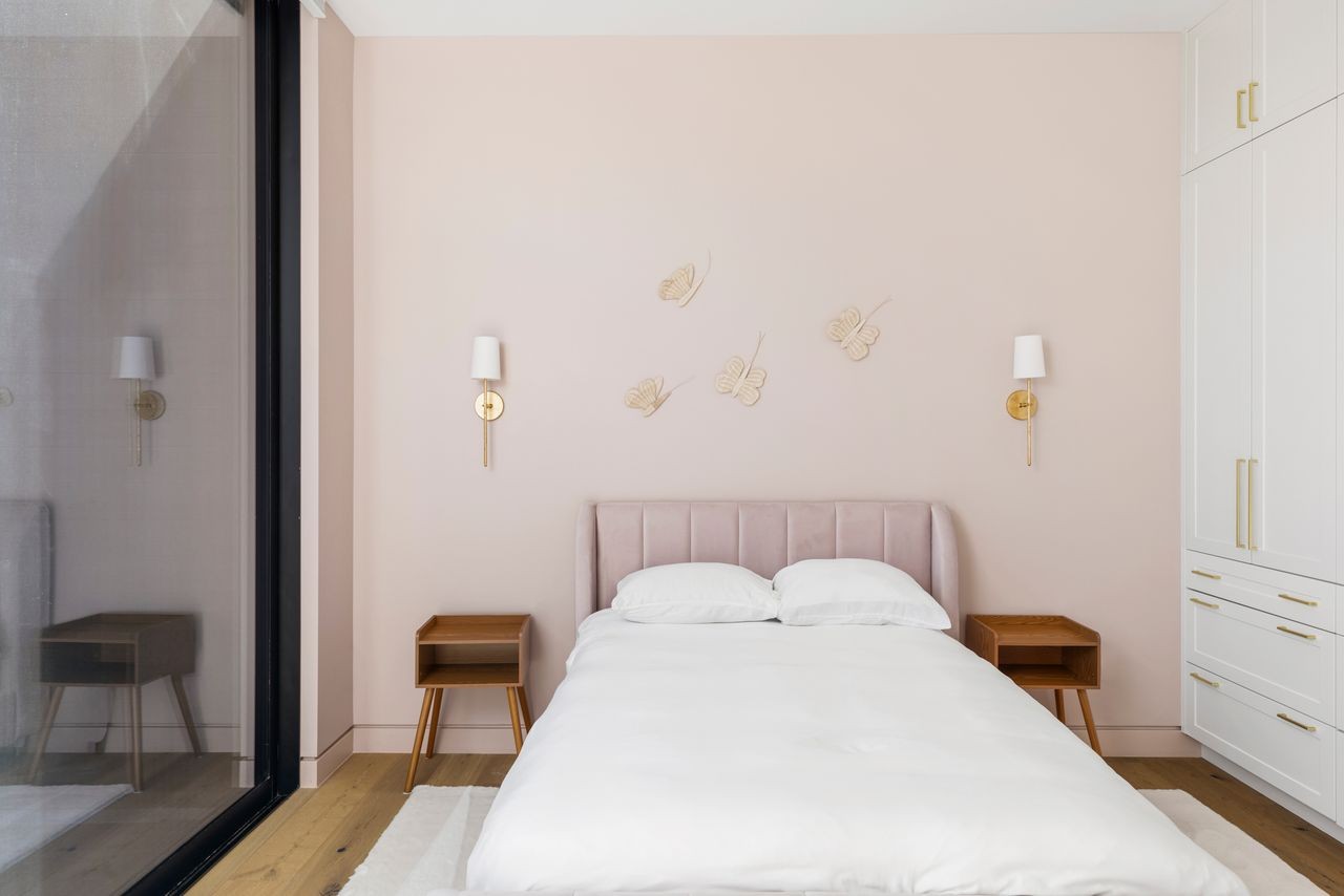 Second guest bedroom introduces a softer tone with blush walls, warm wood accents, and brass sconces framing the bed. 