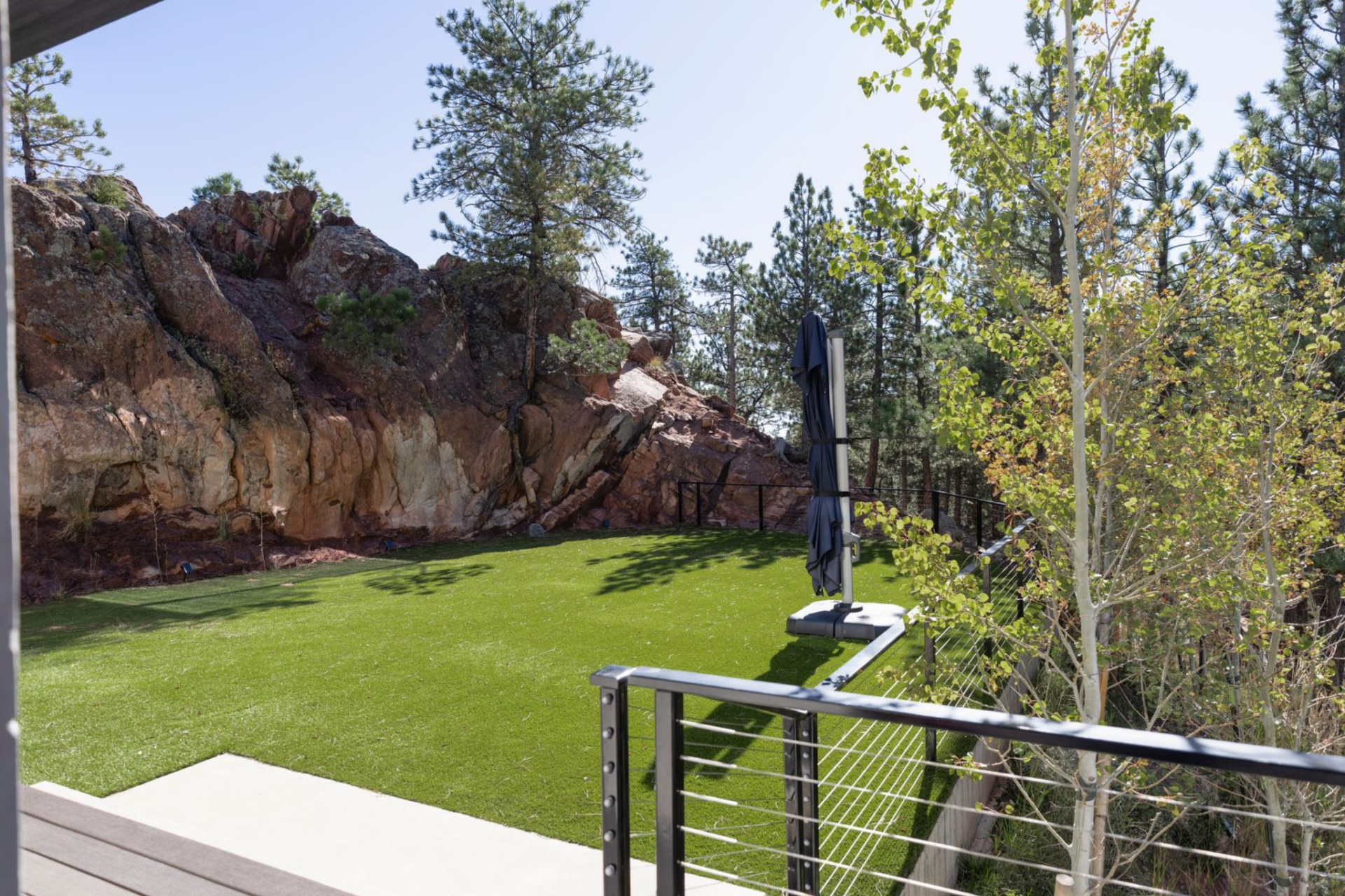 The west-facing flat yard is set into the natural terrain, bordered by dramatic rock outcroppings and trees that give the space privacy. 