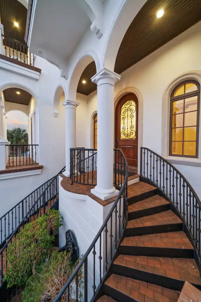 A curved staircase guides you up to the arched front door, where wrought-iron detailing is set into warm wood.