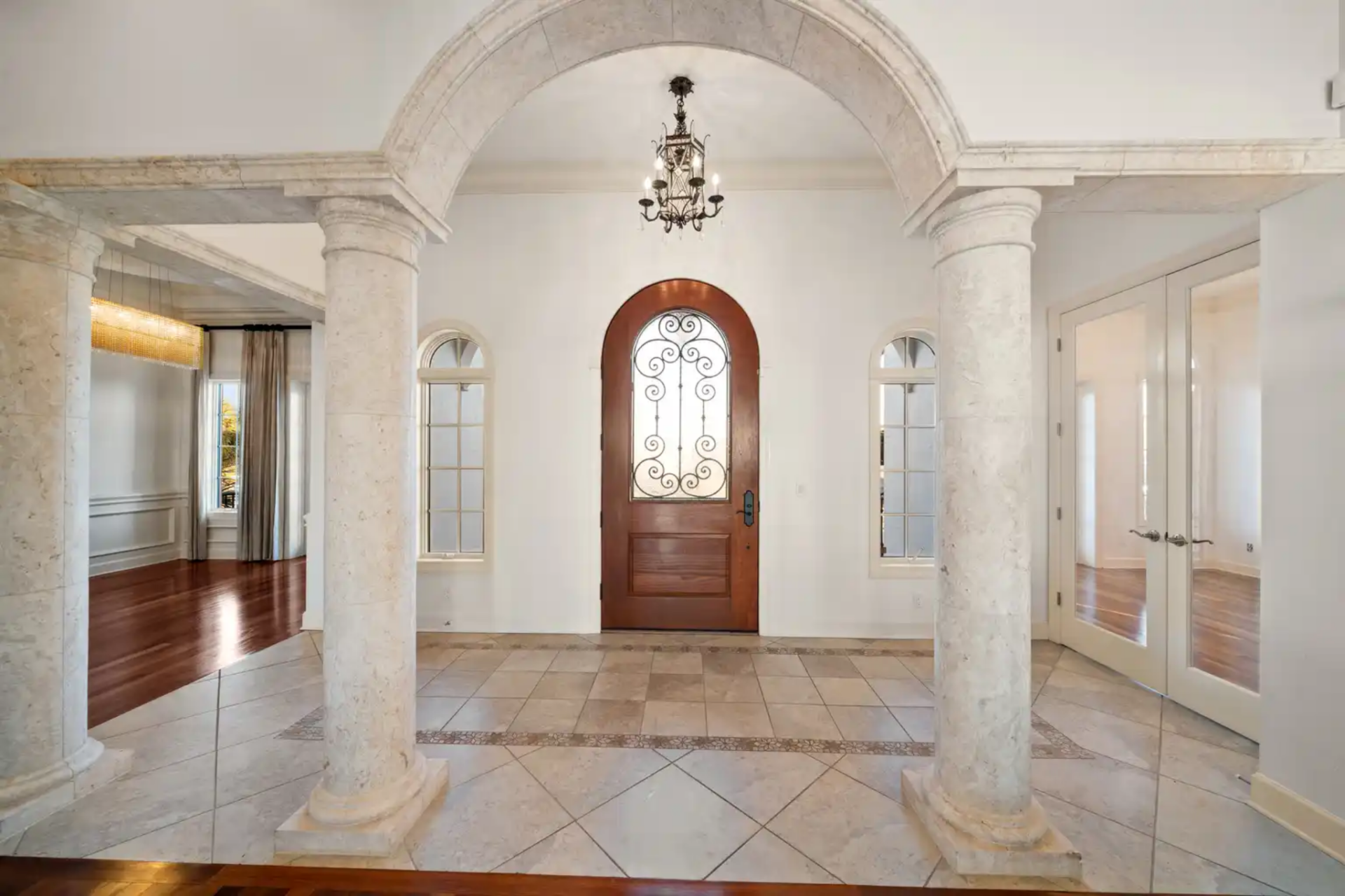 The foyer opens wide with marble and natural stone flooring underfoot, framed by thick columns and arched openings.