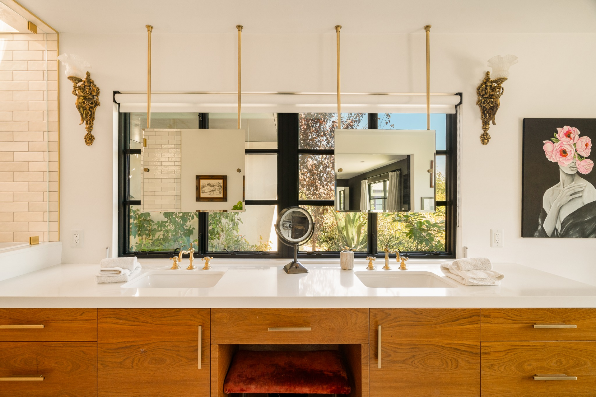 The primary bathroom is designed with a clean, tailored feel, where a long custom vanity stretches beneath twin mirrors suspended from the ceiling, reflecting both light and the suite's bedroom.