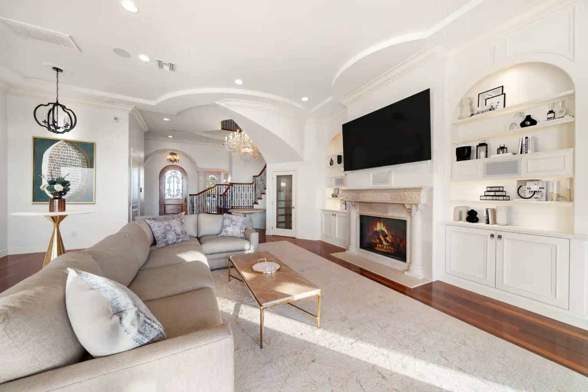 As you step into the living room, the space opens wide with a gas fireplace sitting beneath a mounted TV, which is framed by built-in shelving niches.