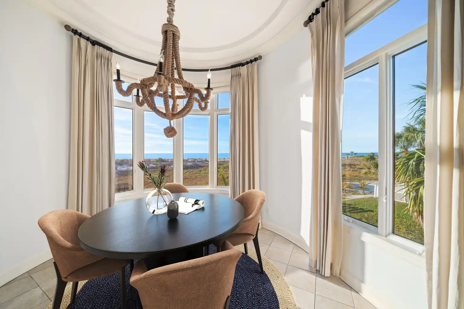 The breakfast nook is wrapped in a curved wall of windows where in the center, a round table with four chairs sits beneath a rope chandelier