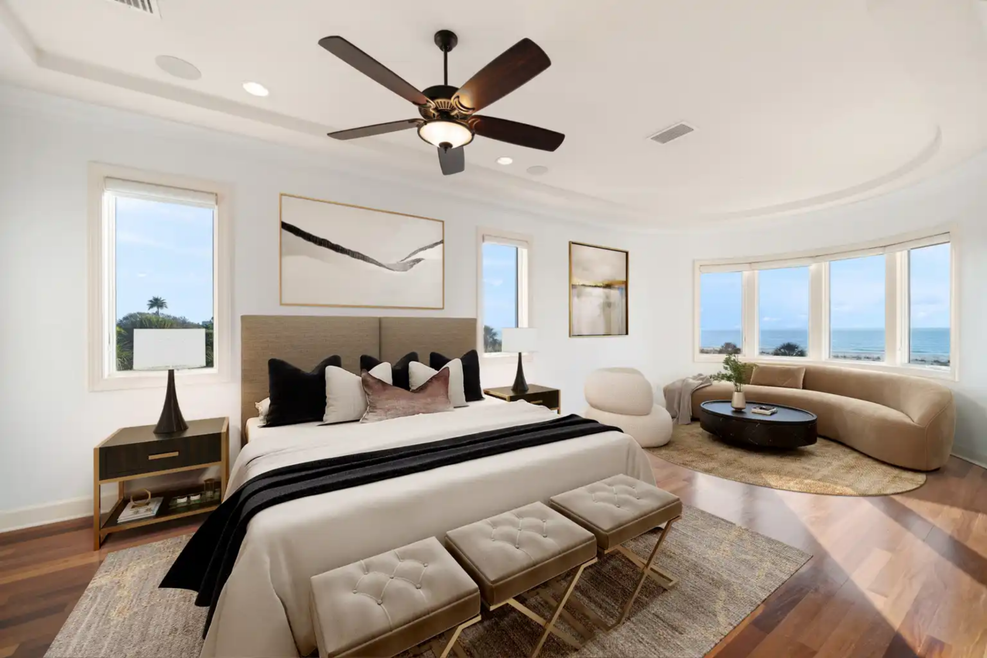 Primary bedroom with a bed beneath a ceiling fan and a sitting area in the corner beneath curved windows.