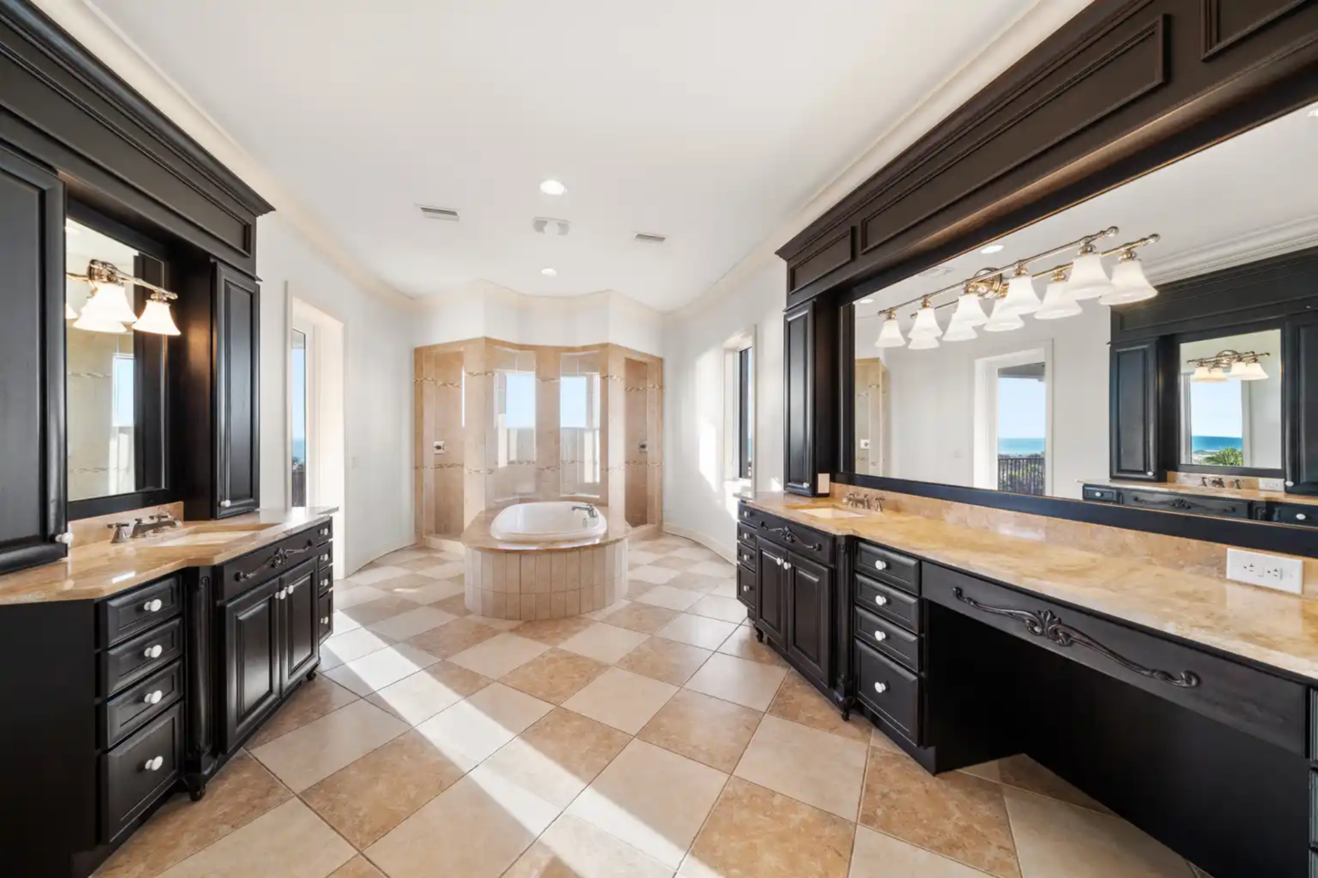 The en-suite bath continues the luxury of the suite, with dual vanities lining opposite walls, finished in dark cabinetry and stone countertops that contrast cleanly with the lighter marble flooring.