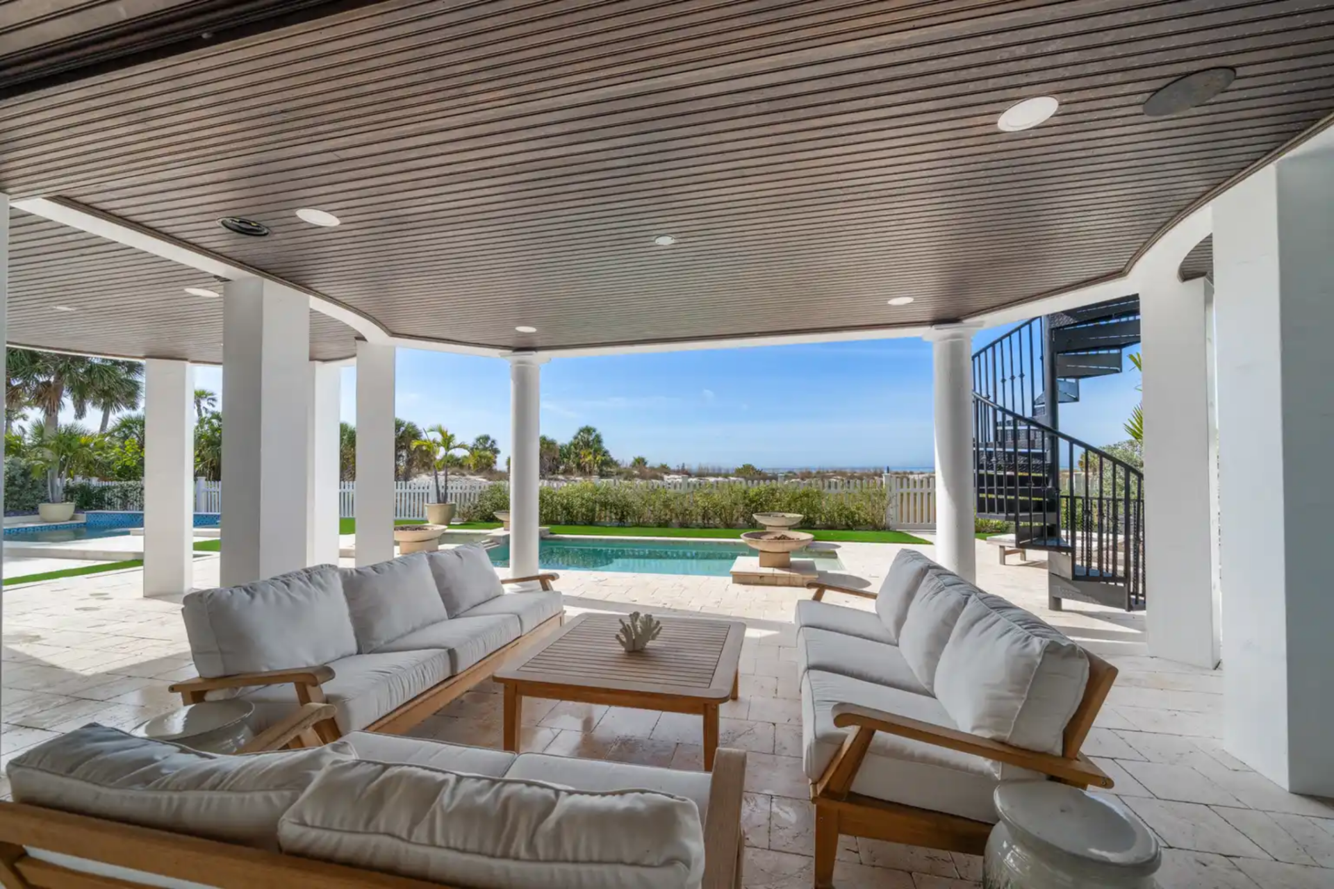 A columned patio consists of multiple seating zones, with a wood-paneled ceiling, recessed lighting, and room for lounging.