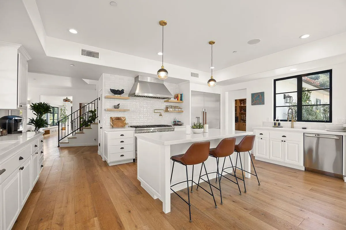 Just down the hall, the kitchen continues the bright interiors with a long white island with waterfall edges and three leather-seated stools lined neatly along one side.
