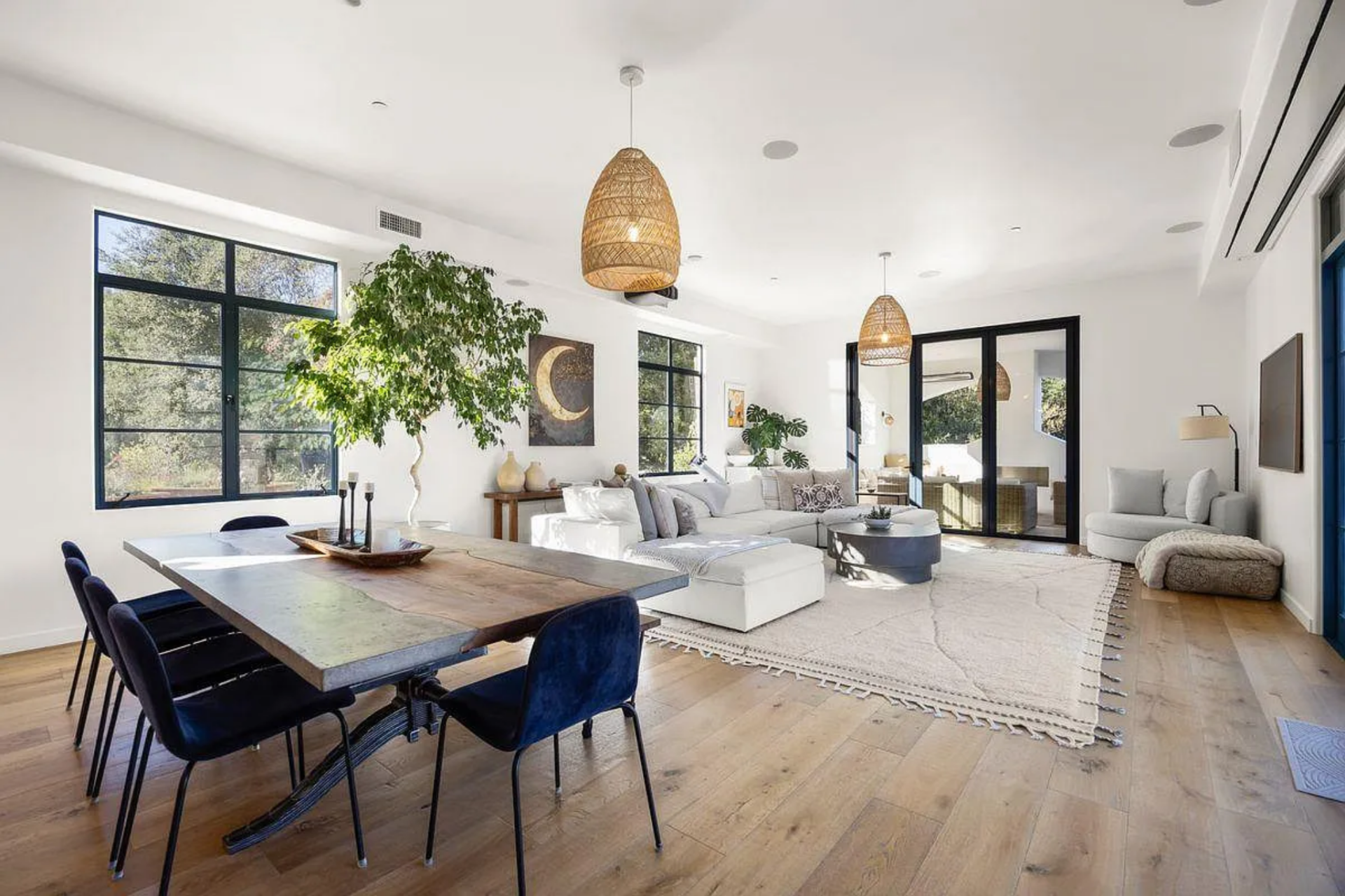 The dining area comes first, featuring a long rectangular wood table surrounded by dark blue velvet chairs on three sides and a bench on the fourth.