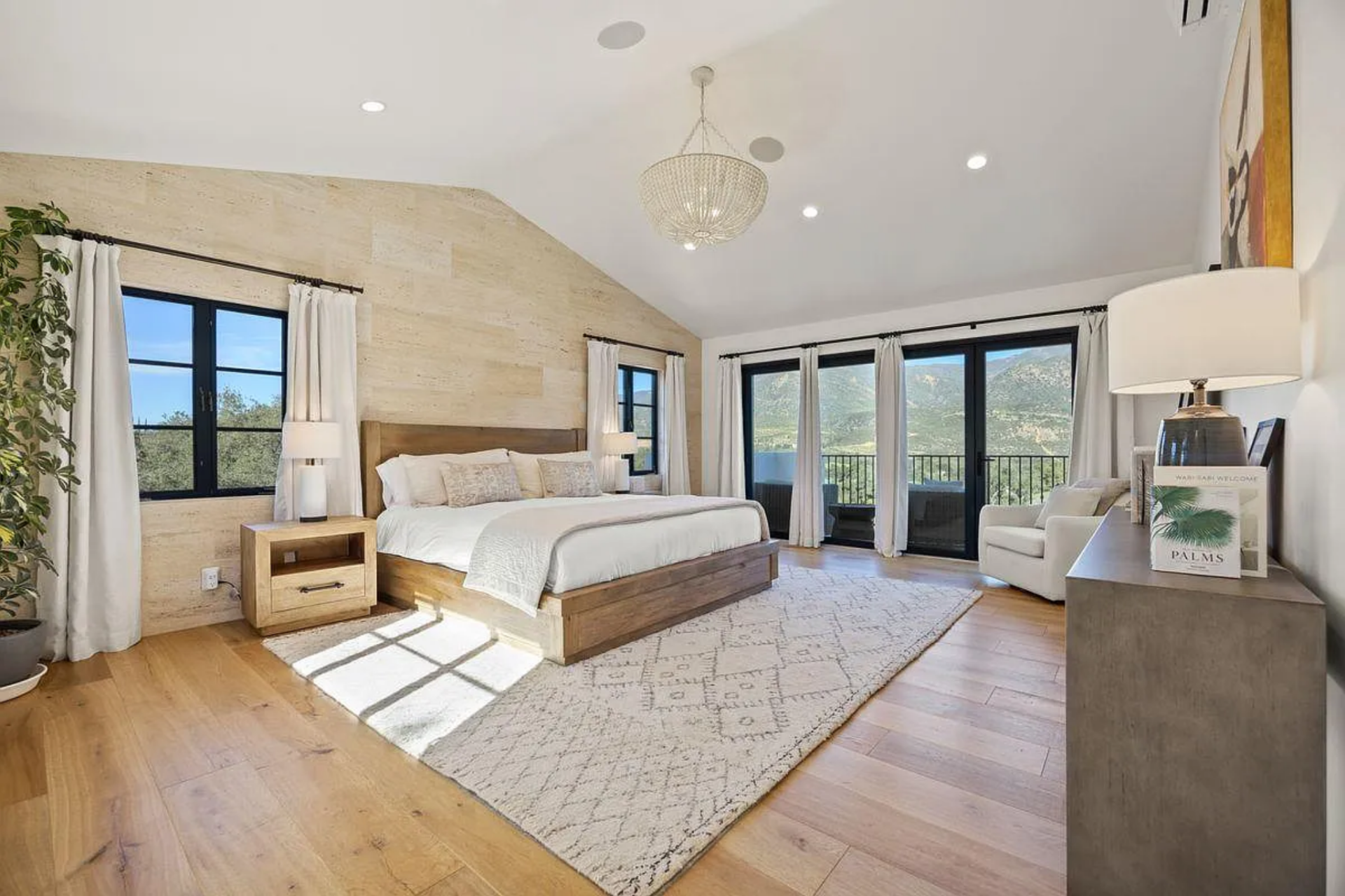 The primary suite's bedroom centers around a low, solid wood bed frame set against a full-height travertine accent wall.