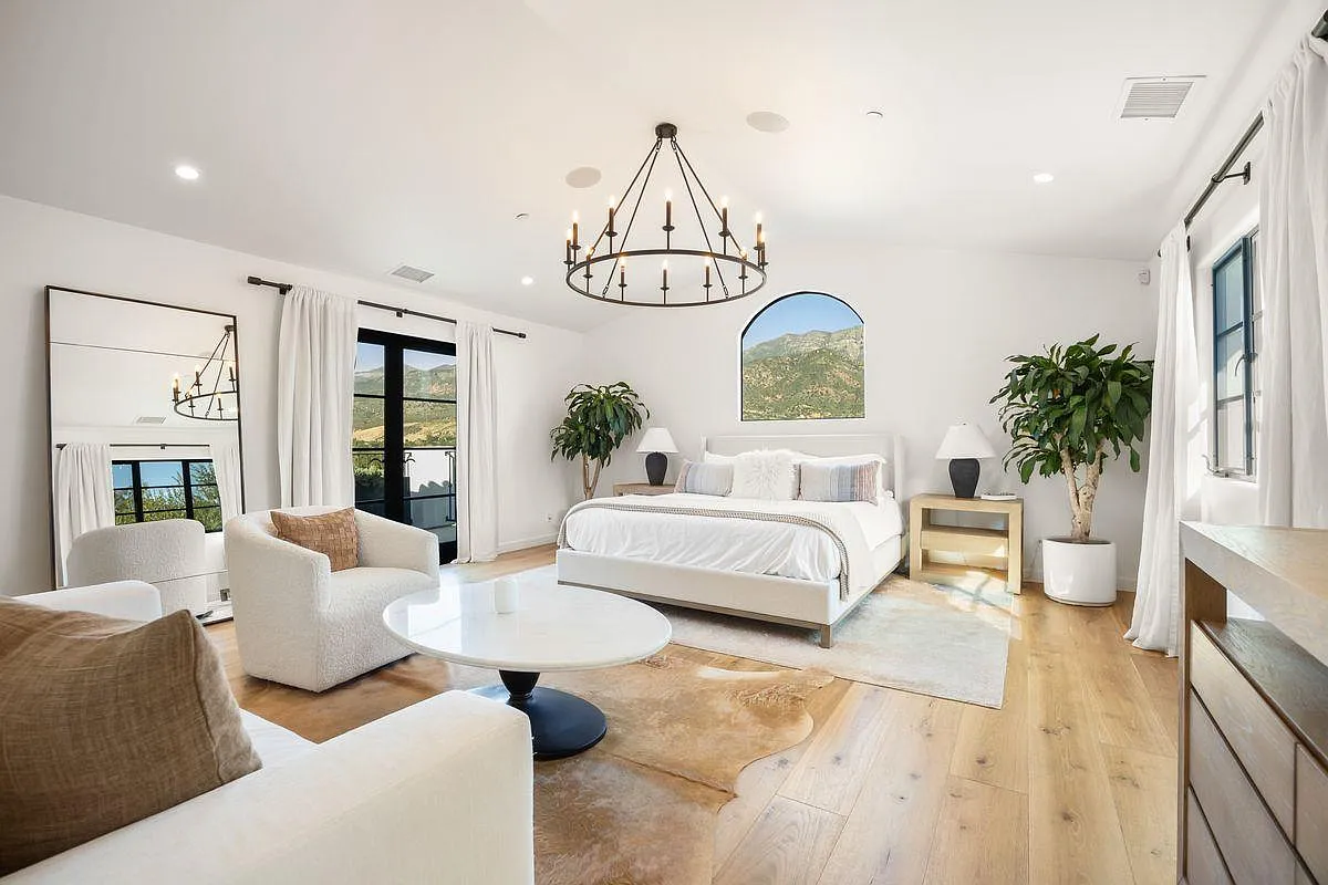 The bedroom is set up as a calm, well-proportioned space with wide plank wood floors running wall to wall and black-framed windows bringing in natural light.