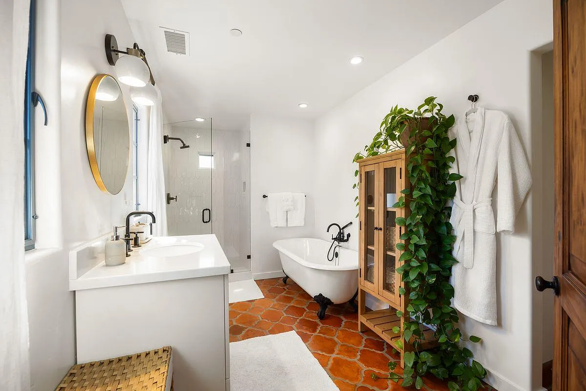 A glass-enclosed shower and a freestanding soaking tub sits just beyond the vanity, which features a simple white countertop, integrated sink, and modern fixtures.