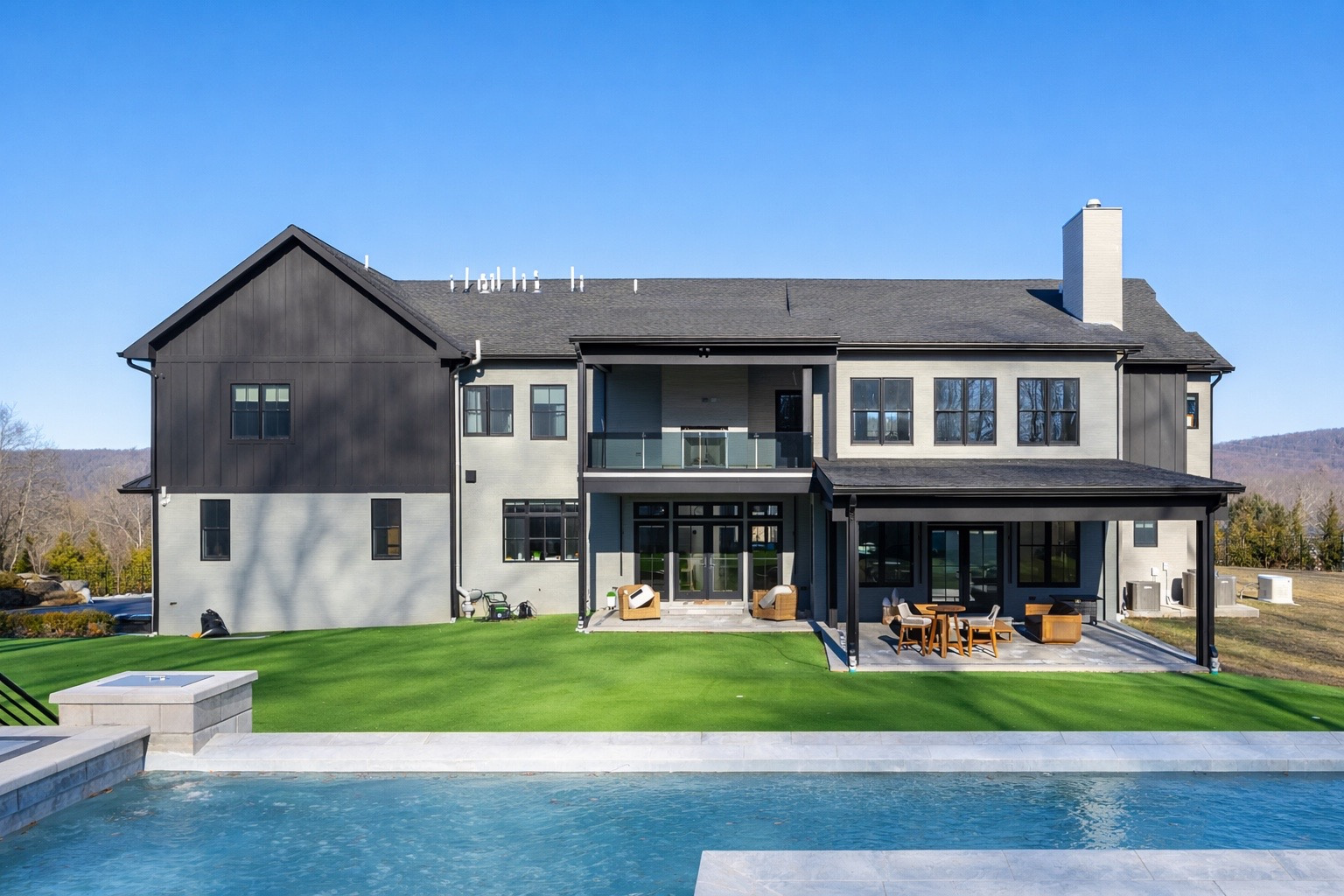 Around the corner from the front entrance, the backyard opens with a covered patio that acts as a natural extension of the home, offering shaded seating and direct views of the raised infinity pool.