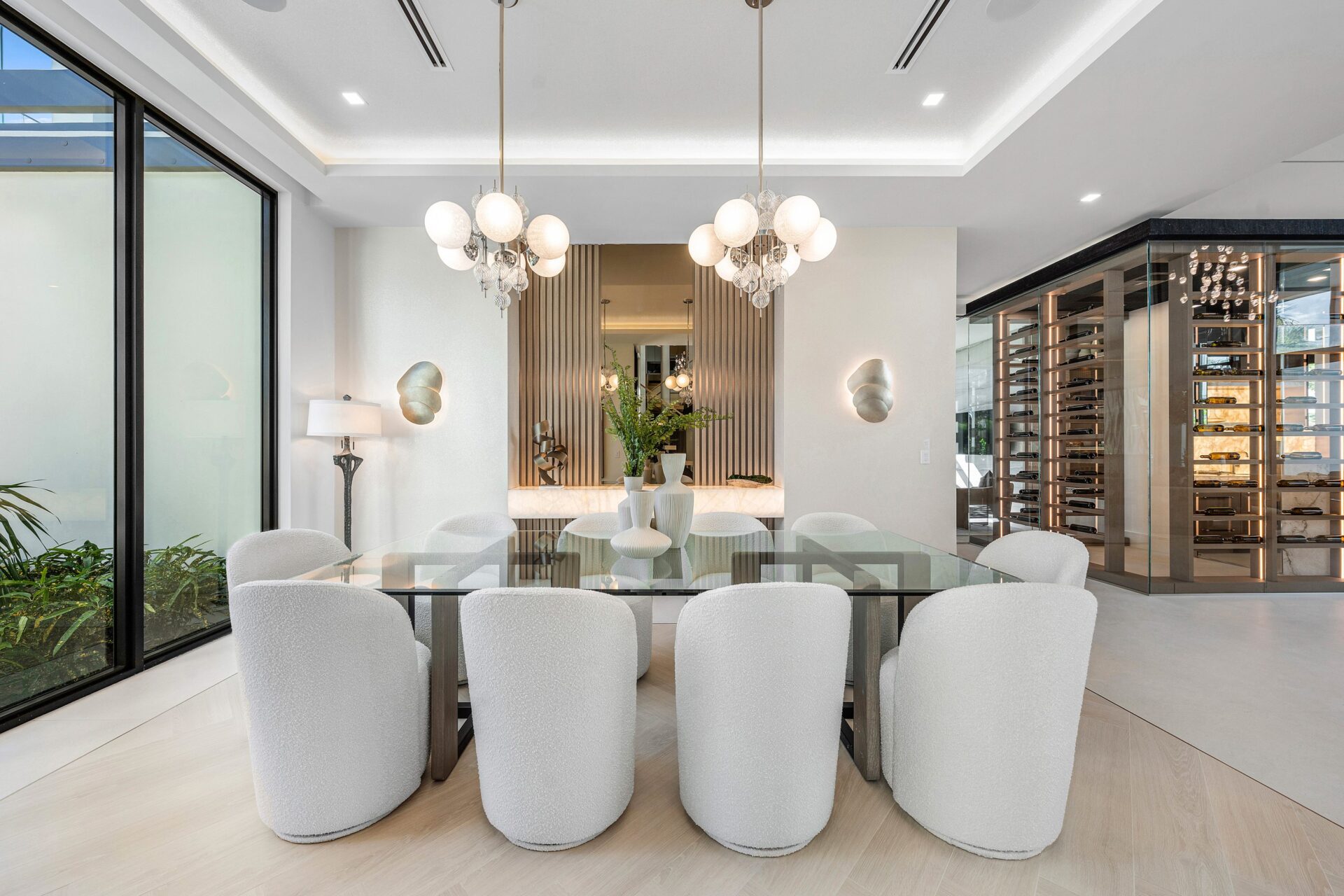A few steps from the wine room, the formal dining area features a long glass-top table surrounded by rounded upholstered chairs, all beneath a pair of hanging sculptural pendant lights.