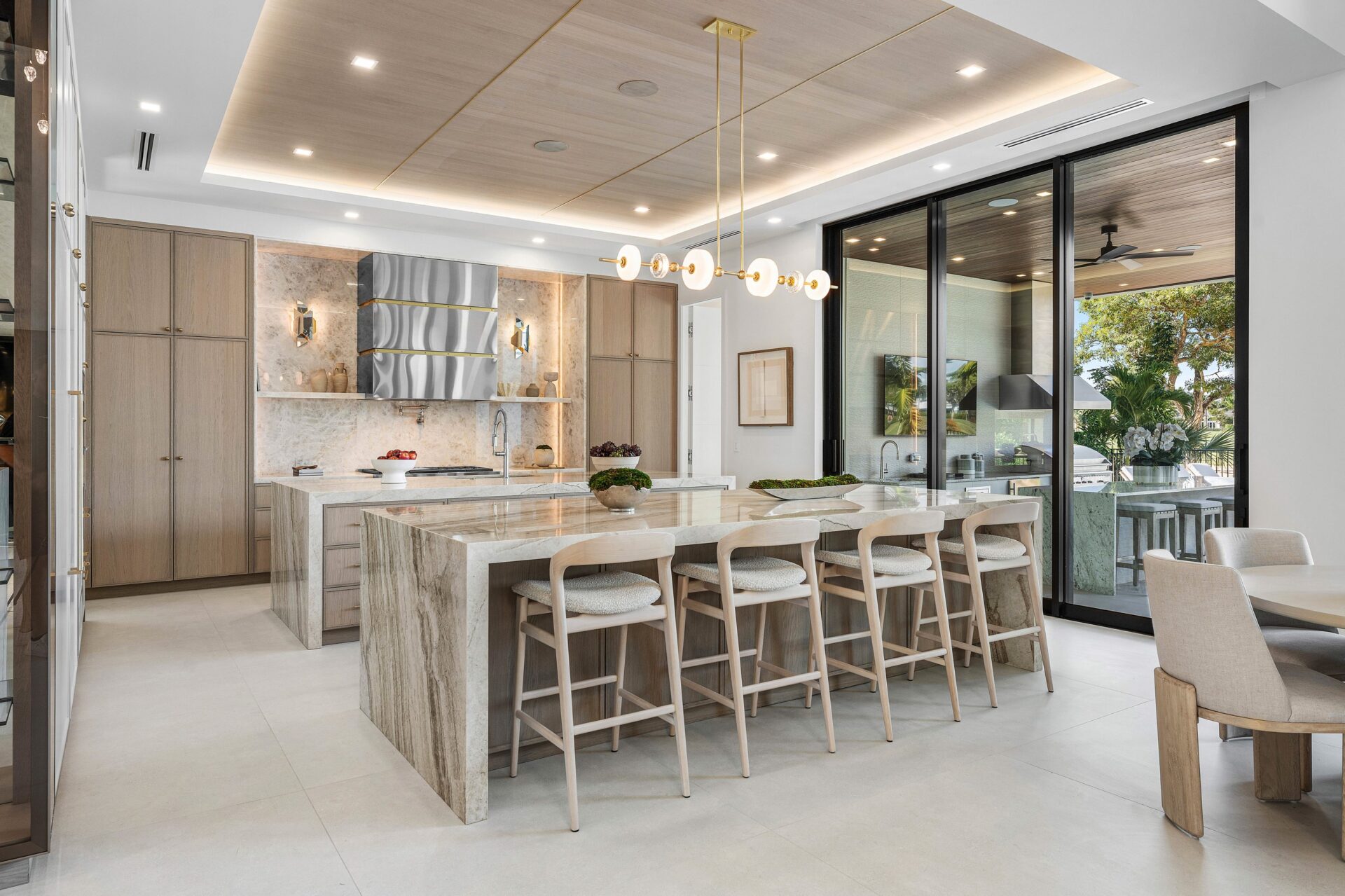 Custom cabinetry runs wall to wall in a soft wood finish, while the stone surfaces and integrated appliances keep the palette clean and consistent with the rest of the house.