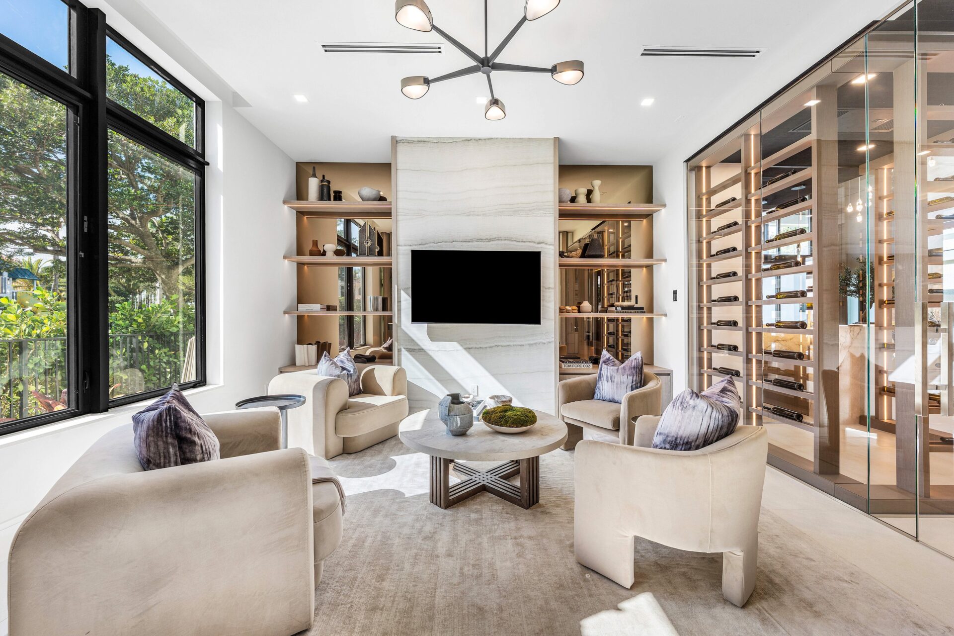 Four lounge chairs are arranged around a round table, creating a clear conversation circle centered on the built-in media wall.
