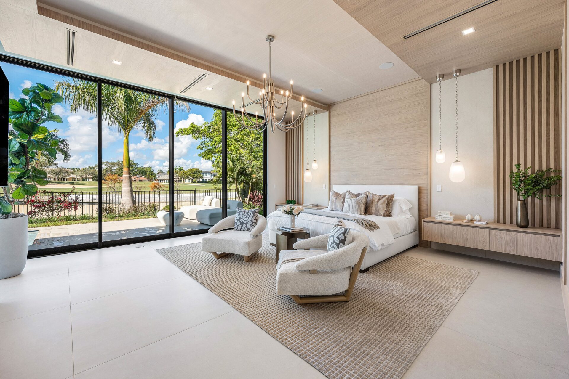 The primary suite on the main level opens with a bed set against a pale wood feature wall and two lounge chairs placed at its foot.