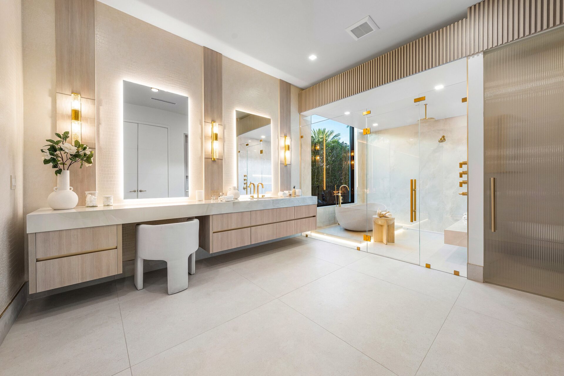 From there, the suite continues into one of the en-suite baths, where a long floating vanity runs wall to wall beneath illuminated mirrors and vertical sconces.
