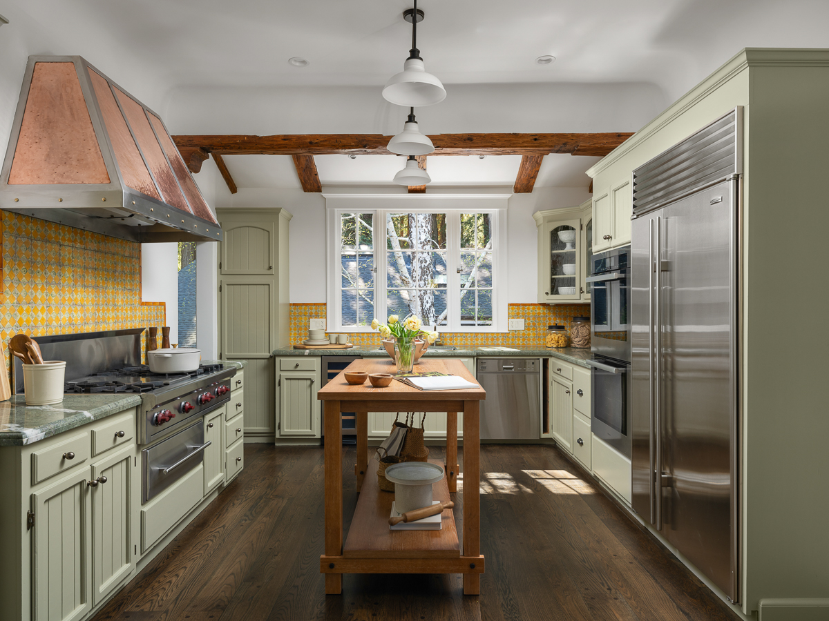  Custom cabinetry lines both sides, while a copper range hood and patterned tile backsplash introduce a layer of texture against the more traditional finishes.