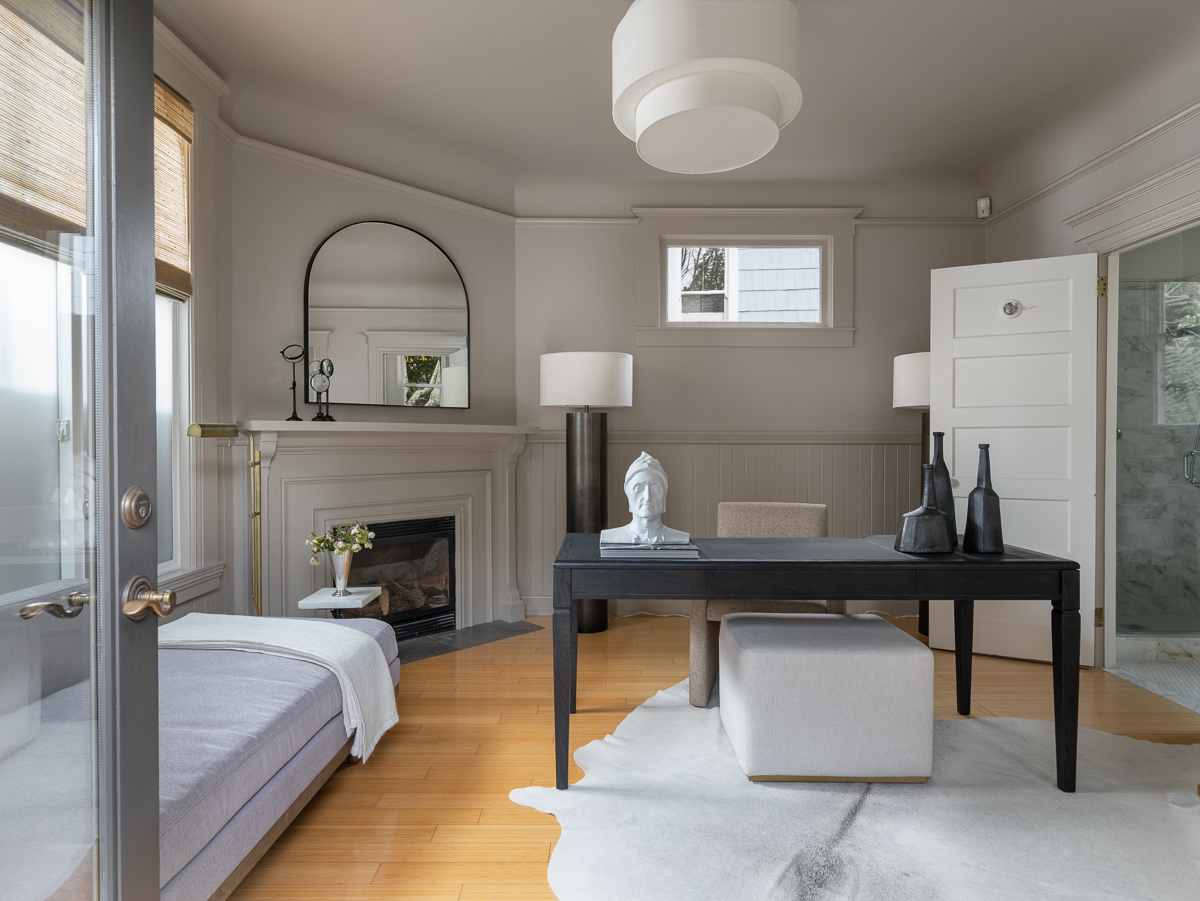 A fireplace sits in the corner, framed by simple molding and topped with a mirror, giving the space a sense of structure without overcomplicating the layout.