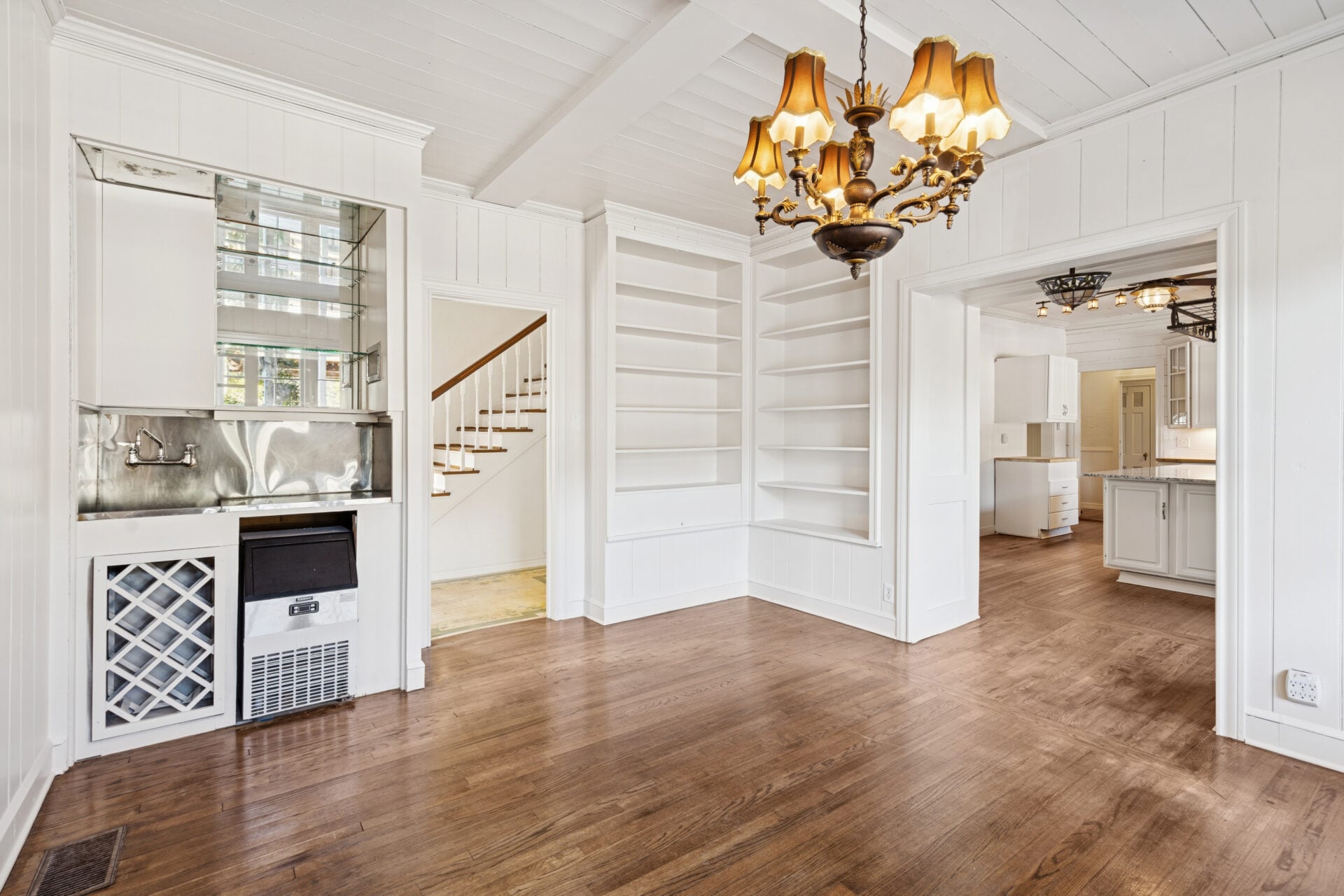 A traditional chandelier hangs above the main dining area, while a built-in wet bar is tucked along one wall, complete with a small sink, storage, and a compact ice maker.
